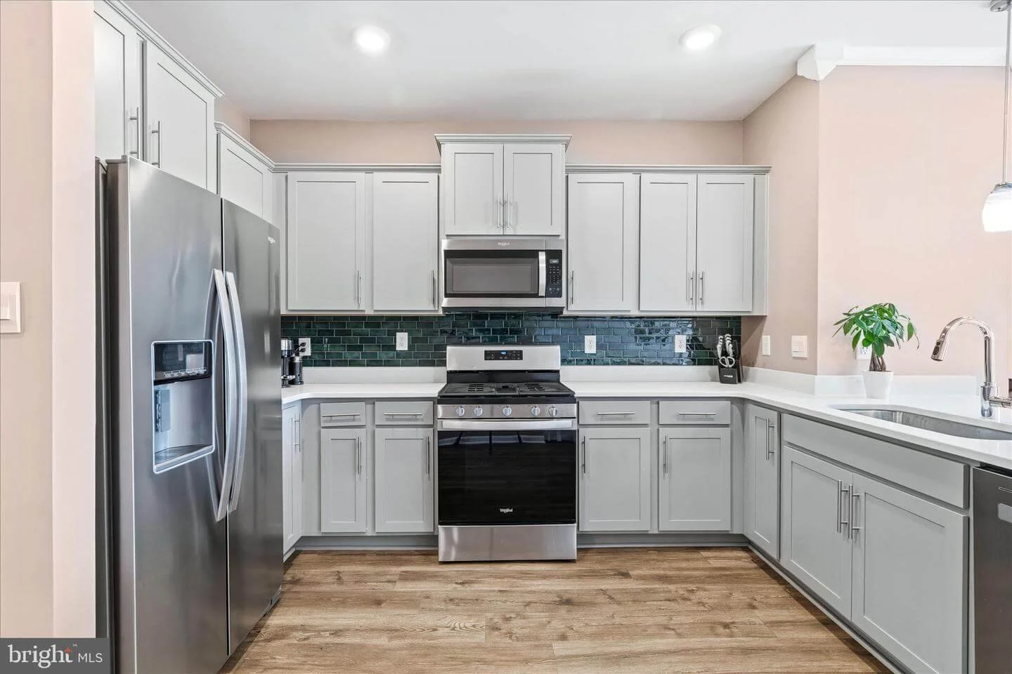 Modern kitchen with gray cabinets, stainless steel refrigerator, microwave, oven, black backsplash, and a potted plant on the counter.