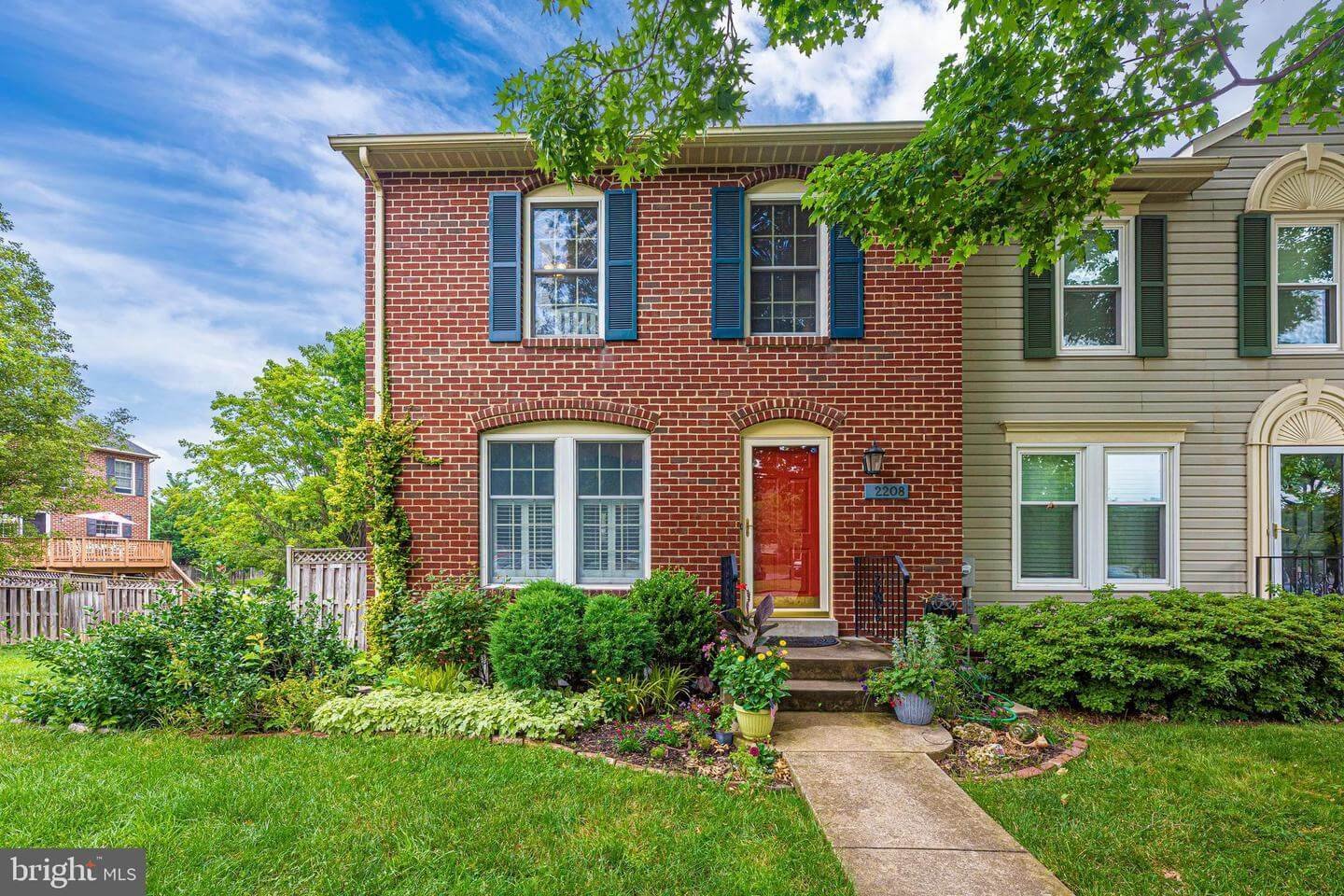 Residence with a red brick exterior, blue shutters, and a red front door, surrounded by a well-maintained green lawn and garden.