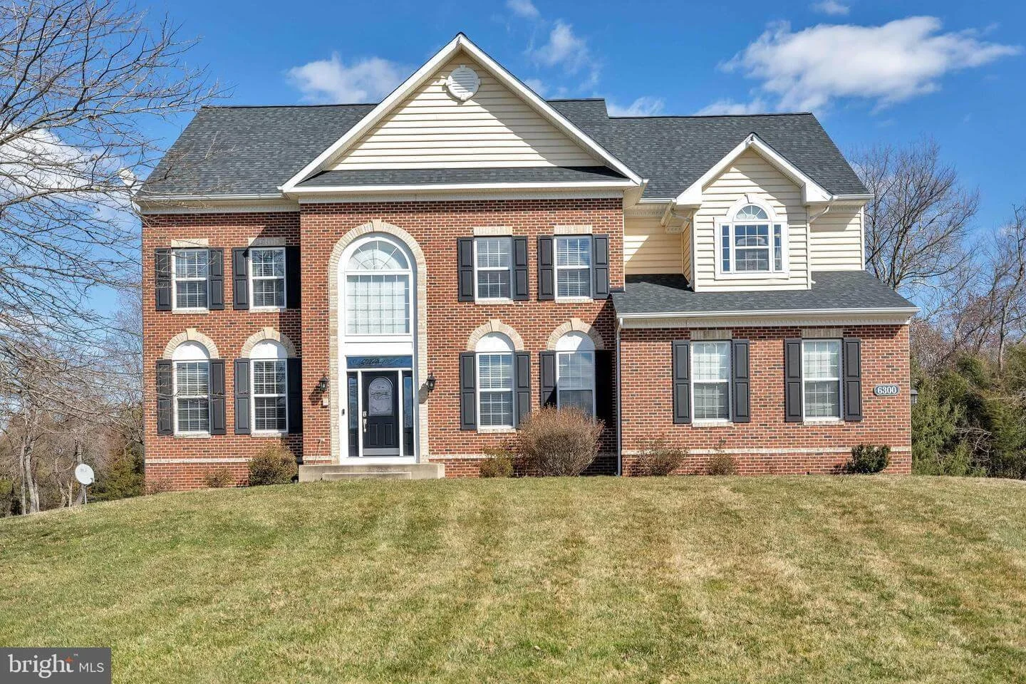 A large two-story house with brick and white siding exterior, multiple windows with black shutters, and a black front door, set on a grassy lawn.