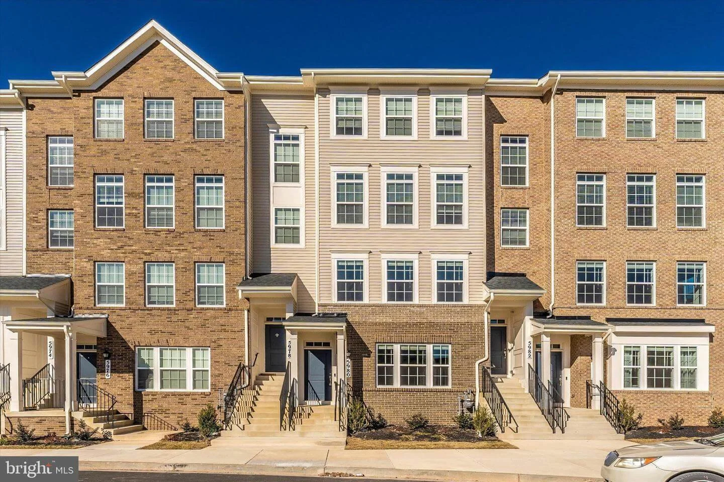 Row of modern brick townhouses with multiple windows and small front steps, under a blue sky.
