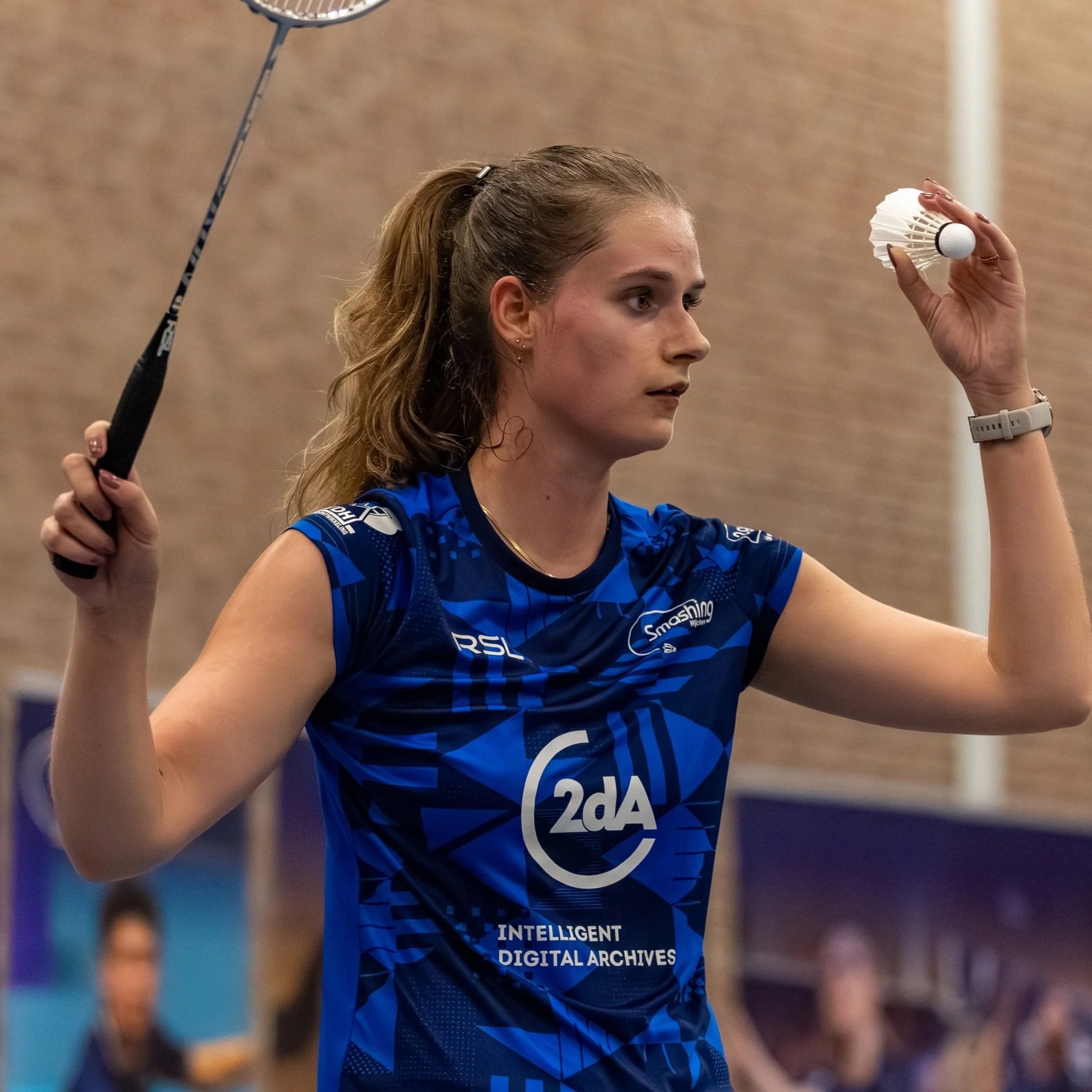 De achterkant van een vrouwelijke tennisser met haar blonde haar in een staart, die zich voorbereidt op een volley op een tennisbaan.