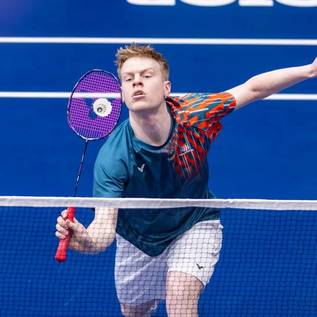 Timo Stoffelen die badminton speelt op een binnenbaan, klaar om te slaan.