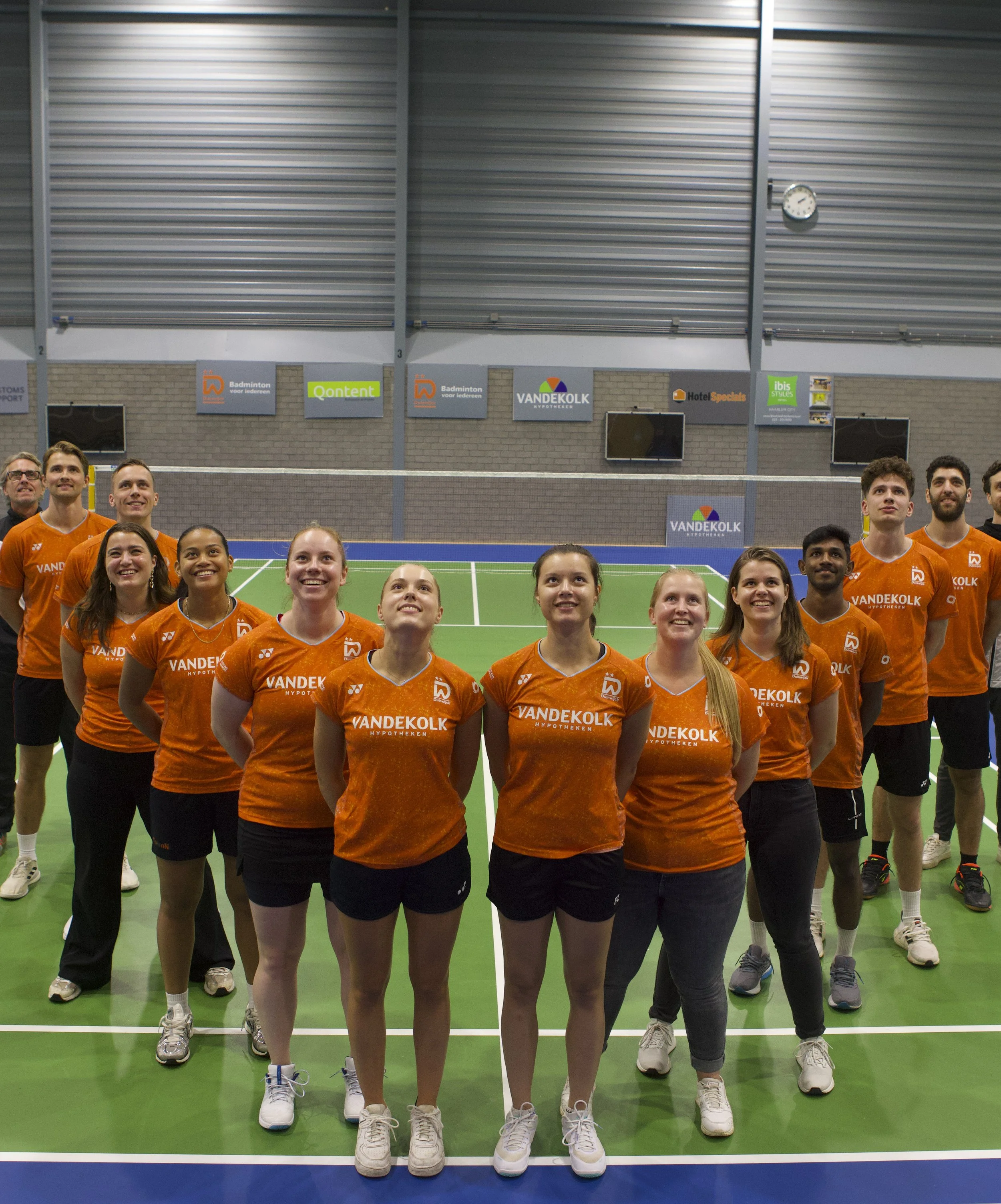 Een groep volleybalspelers in oranje shirts poseert op een indoor volleybalveld.