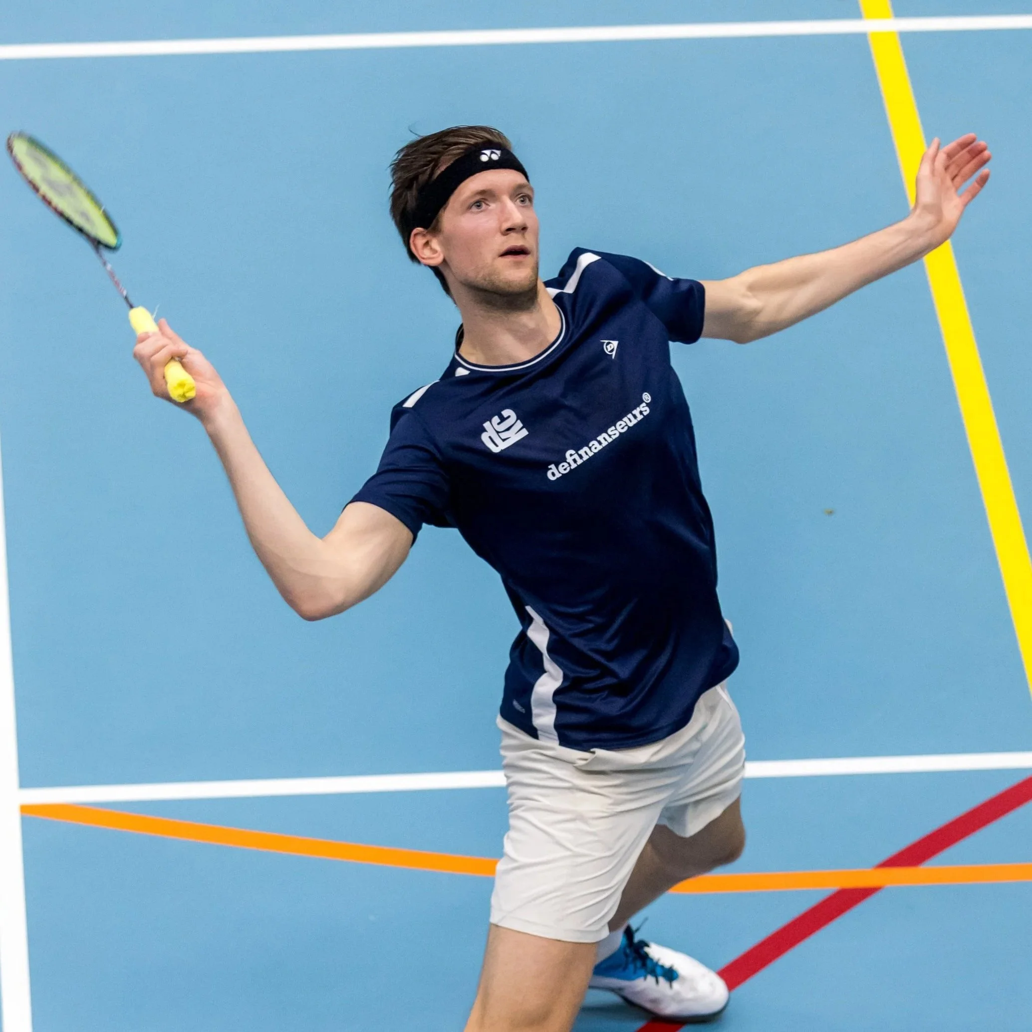 Joran Kweekel in sportkleding die badminton speelt op een blauwe baan met kleurrijke lijnen.