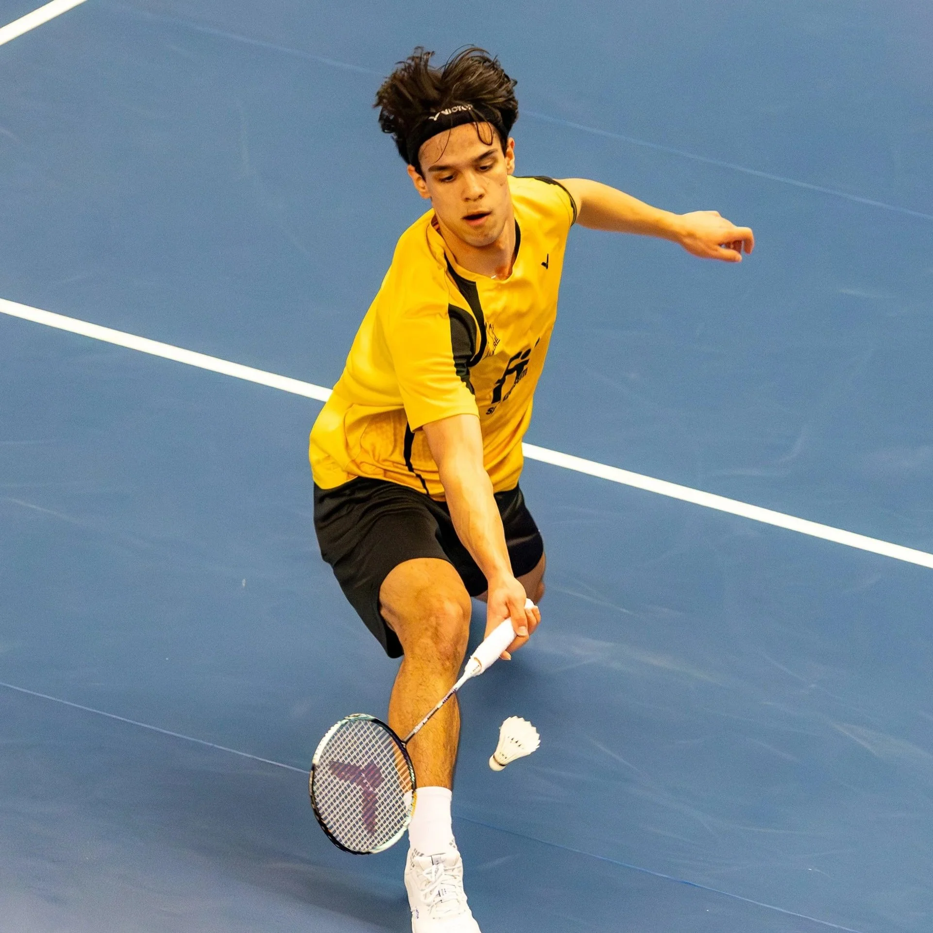 Noah Haase in actie op een badmintonbaan, in zijn clubshirt van BV Almere en slaat een shuttle.