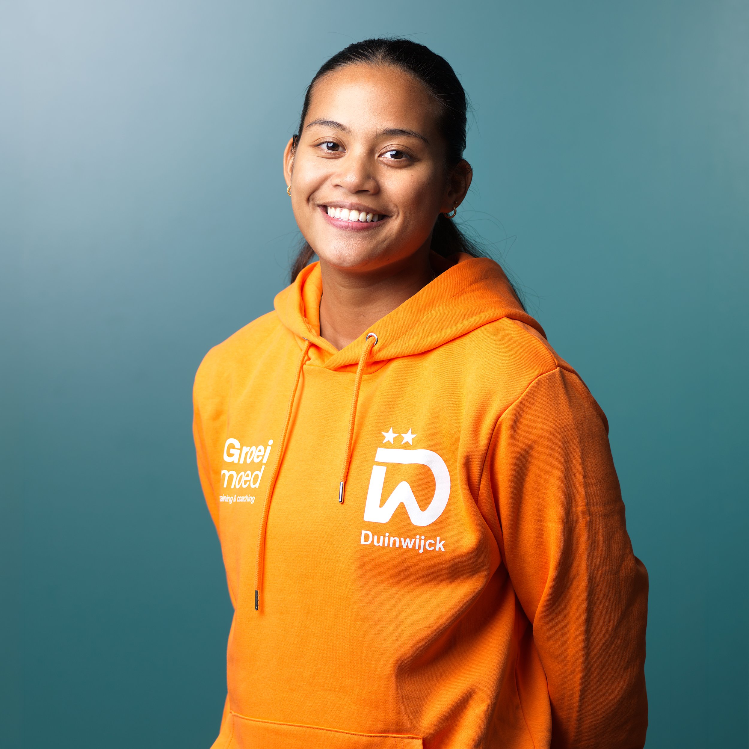 Vrouw in oranje sportshirt met tekst 'Van Dekolk Hypotheken' en logo's, lachend in een sporthal.
