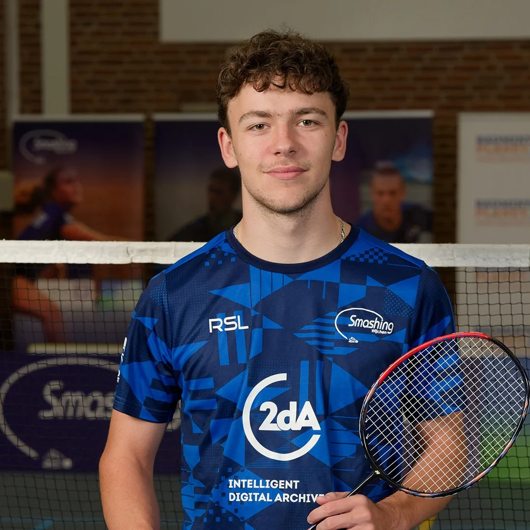 Jonge man in een blauw sportshirt met een tennisracket voor een badmintontafel.