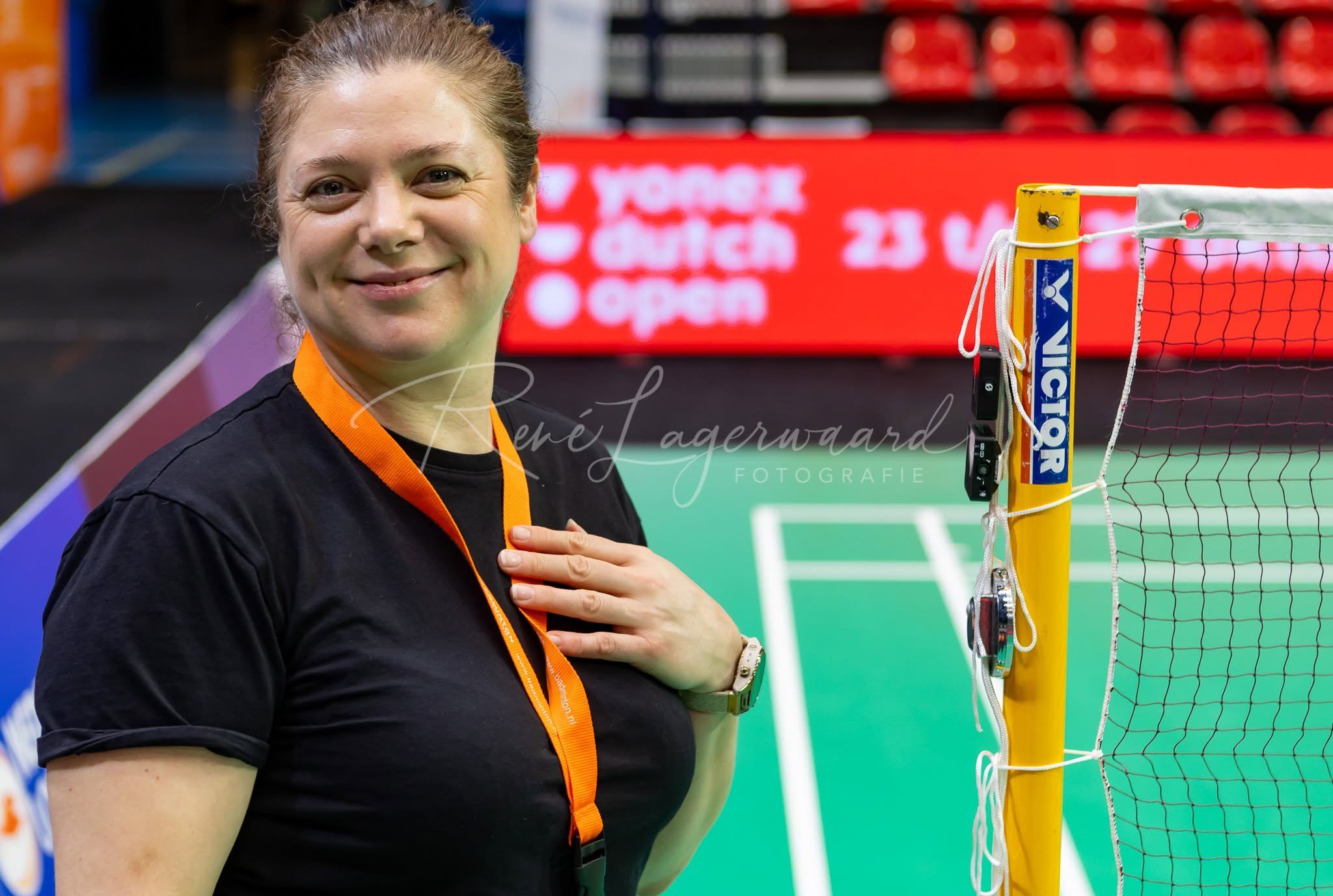 Vrouw die zich verheugt naast een badmintonnet in een sporthal.
