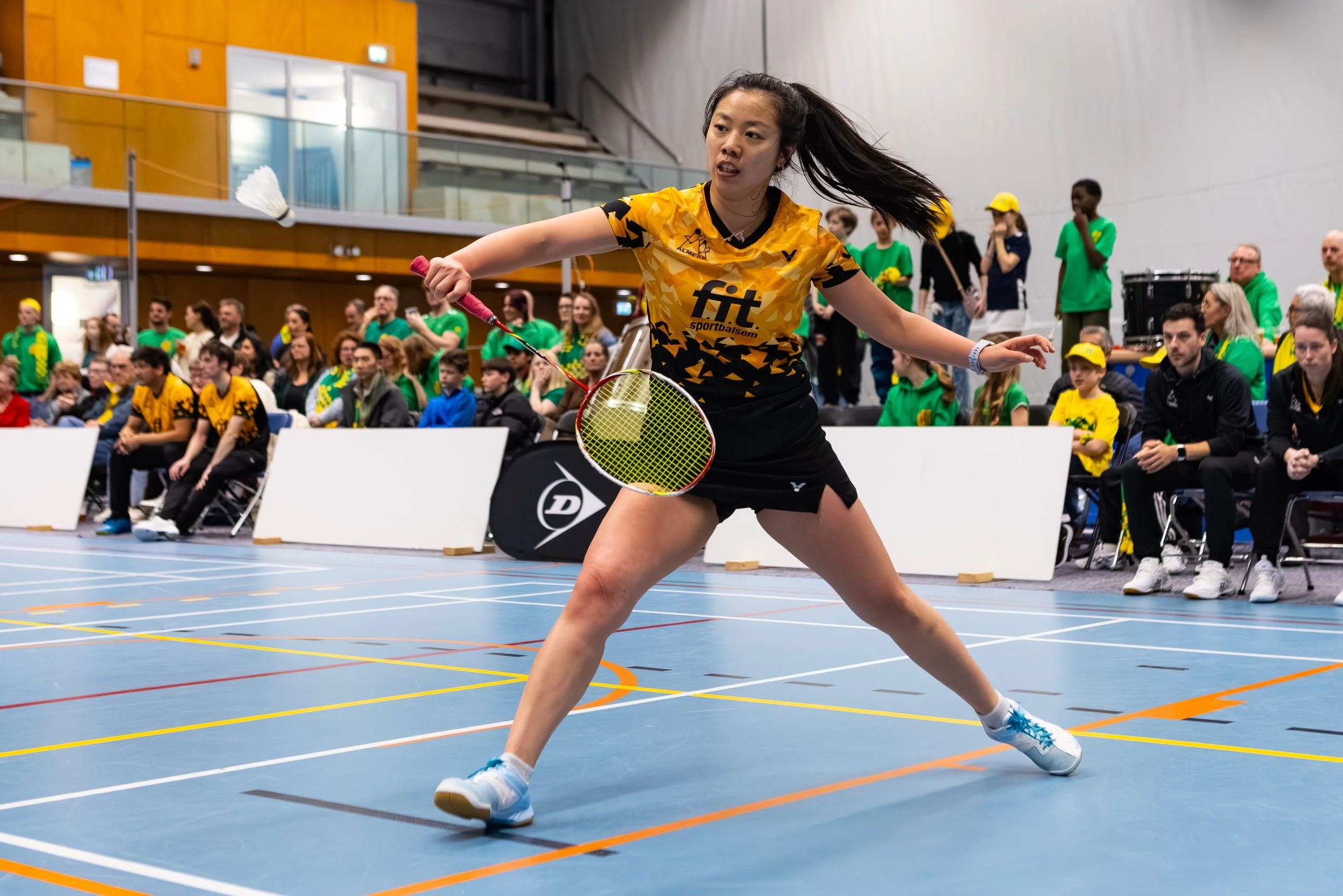 Alida Chen die badminton speelt in een sporthal met een publiek op de achtergrond