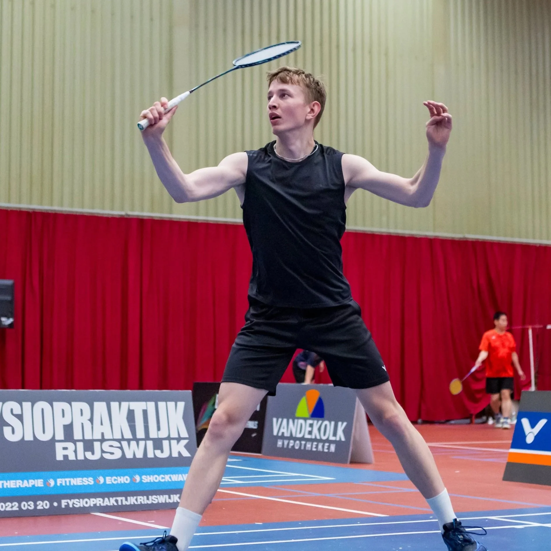 Berend van Brenk met een zwart sportshirt en zwarte korte broek slaat met een racket op een badmintonshuttle op een badmintonbaan bij BC Drop Shot, Mariahoeve Den Haag
