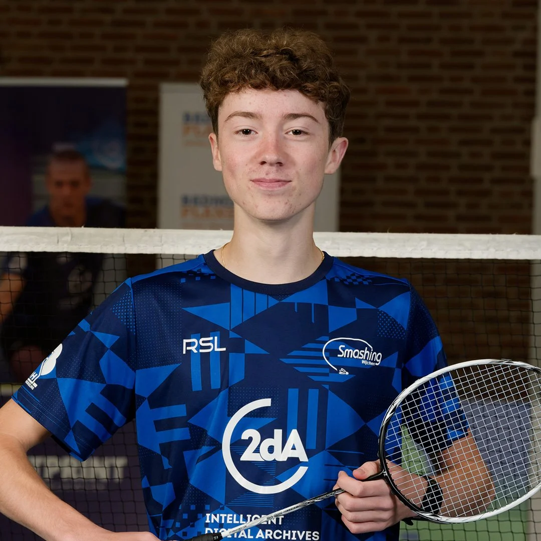Jongeman in blauwe badmintonoutfit met raket voor indoor badmintonbaan.