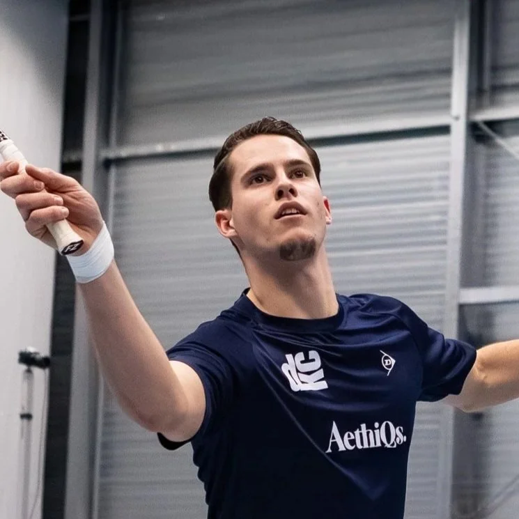Silhouet van een persoon die voor een raam staat, met een achtergrond die een kantoor of schoolomgeving lijkt te zijn.