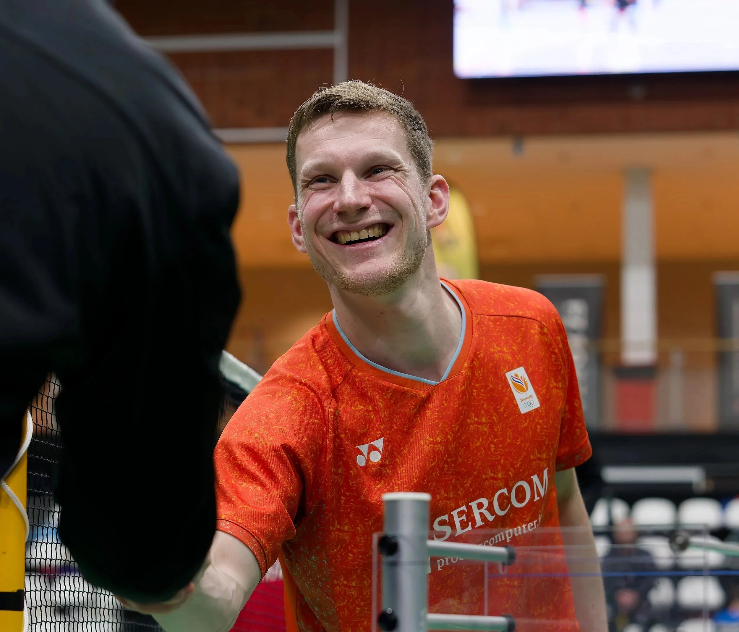Robin Tabeling in een oranje shirt met sportkleding staat in een sportschool of sporthal.