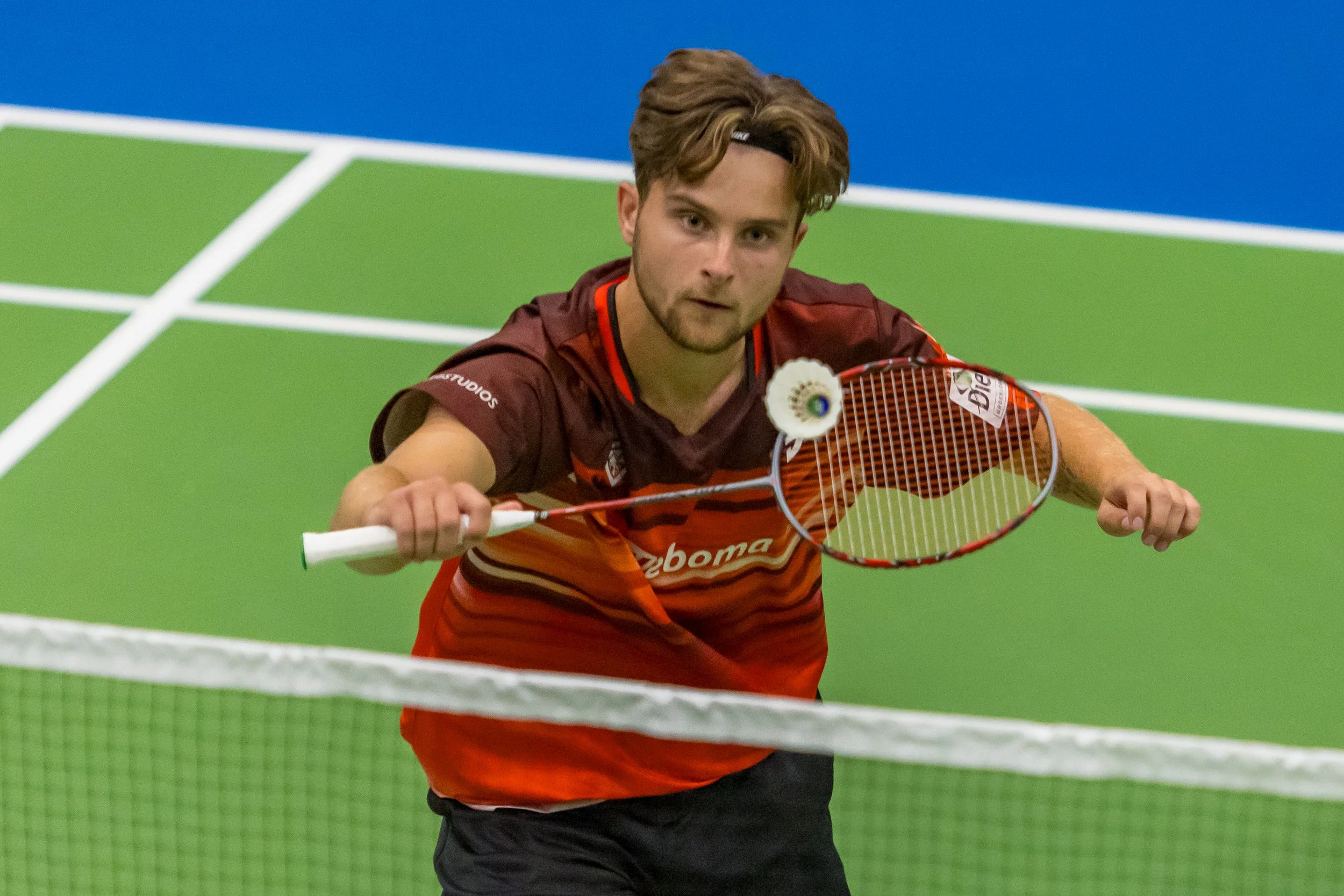 Rens Lagrouw in een rood en zwart sportoutfit met badmintonracket op een indoor badmintonbaan.