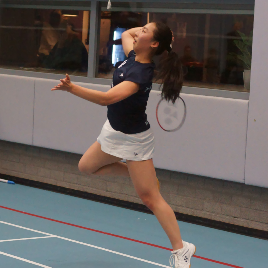 Een jonge vrouw die badminton speelt en springt met een badmintonracket, binnen in een sporthal.