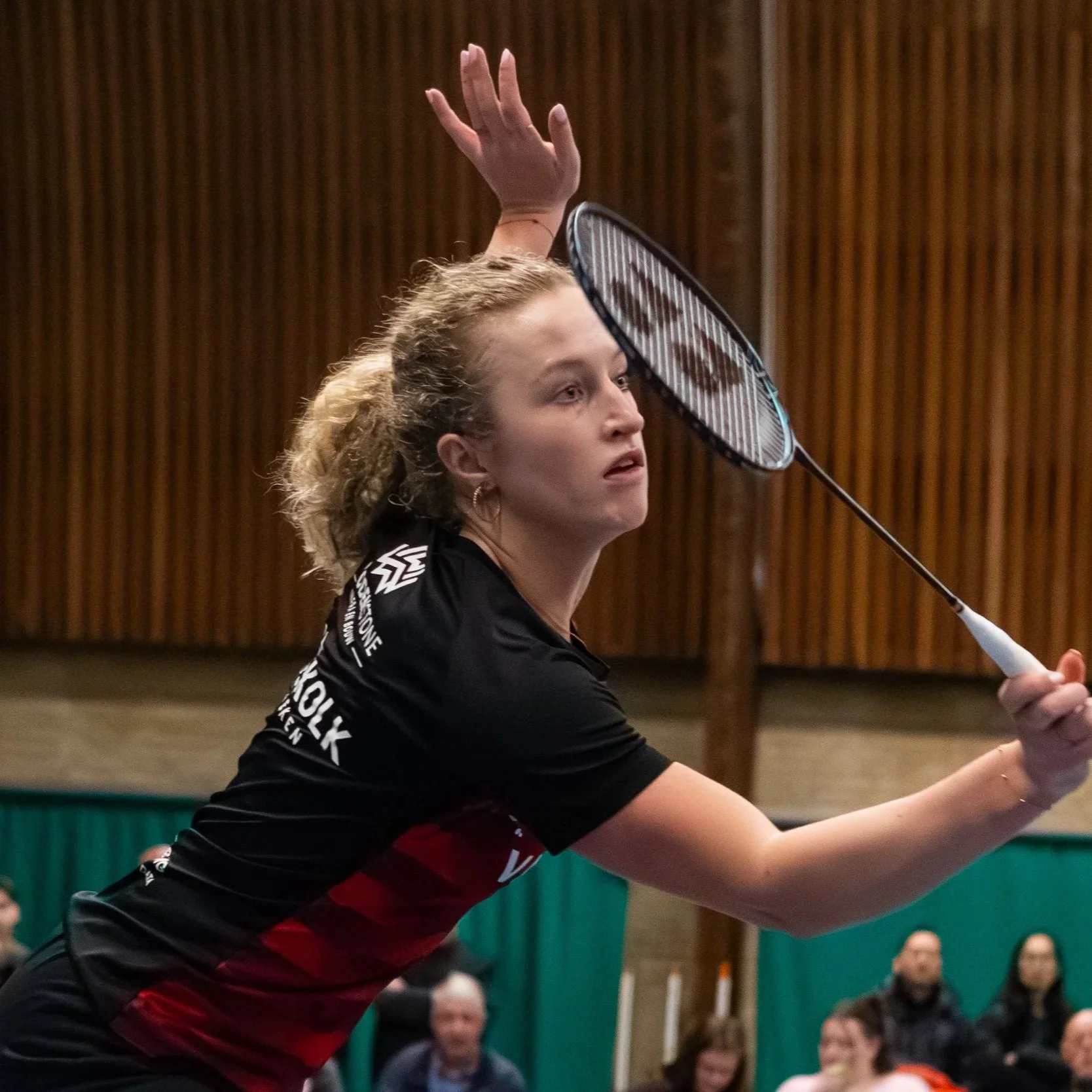 Iris van Leijsen speelt badminton in een sporthal, omringd door toeschouwers.