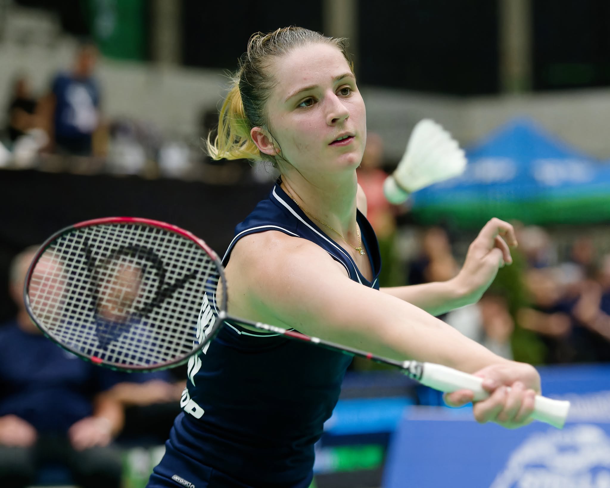 Florentine Schöffski met lang, blond haar in een staart, die een badmintonracket vasthoudt, staat in een sporthal
