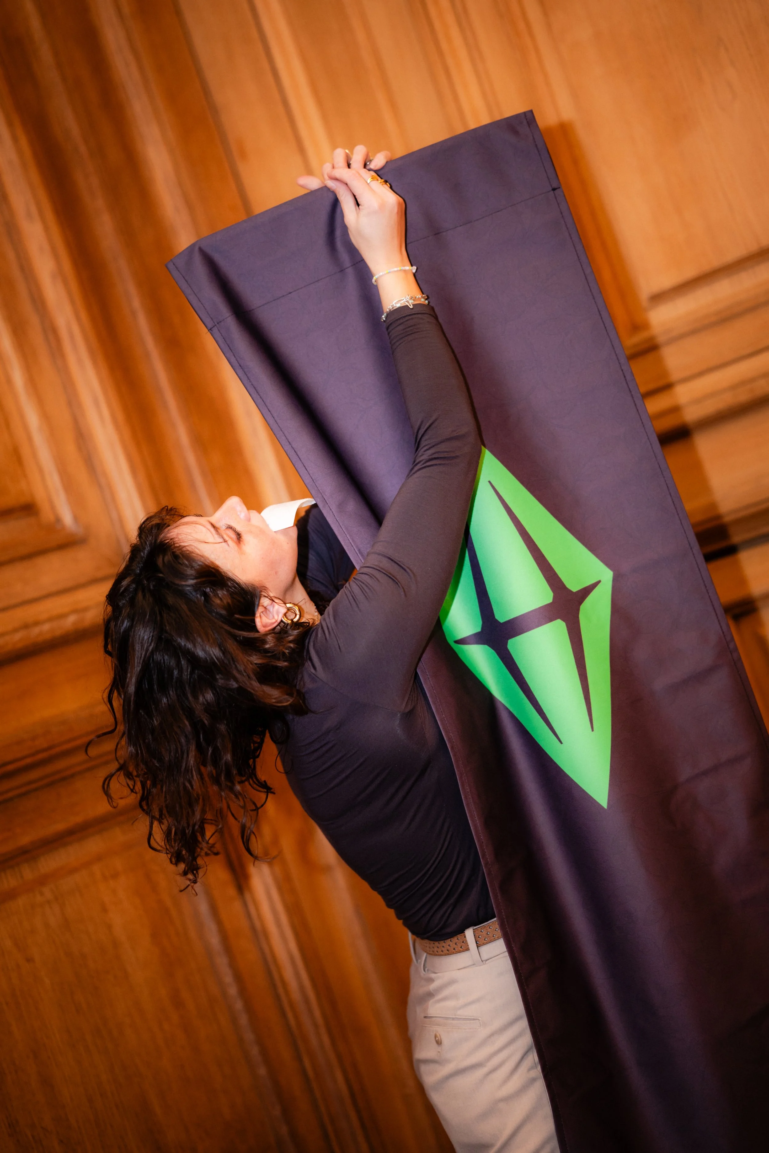 Une femme serre une bannière noire avec un logo vert et noir dans une salle en bois.