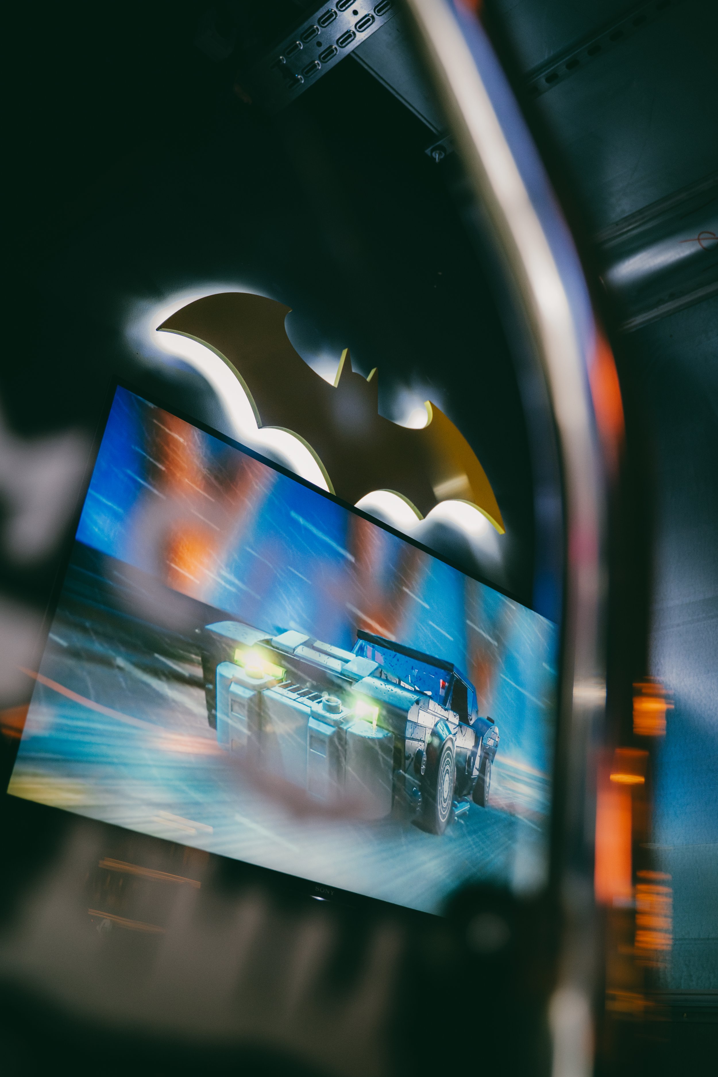 Une affiche de jeu vidéo avec une voiture futuriste sur un fond dynamique, vue floue à travers un cadre ou un objet, avec des effets lumineux.