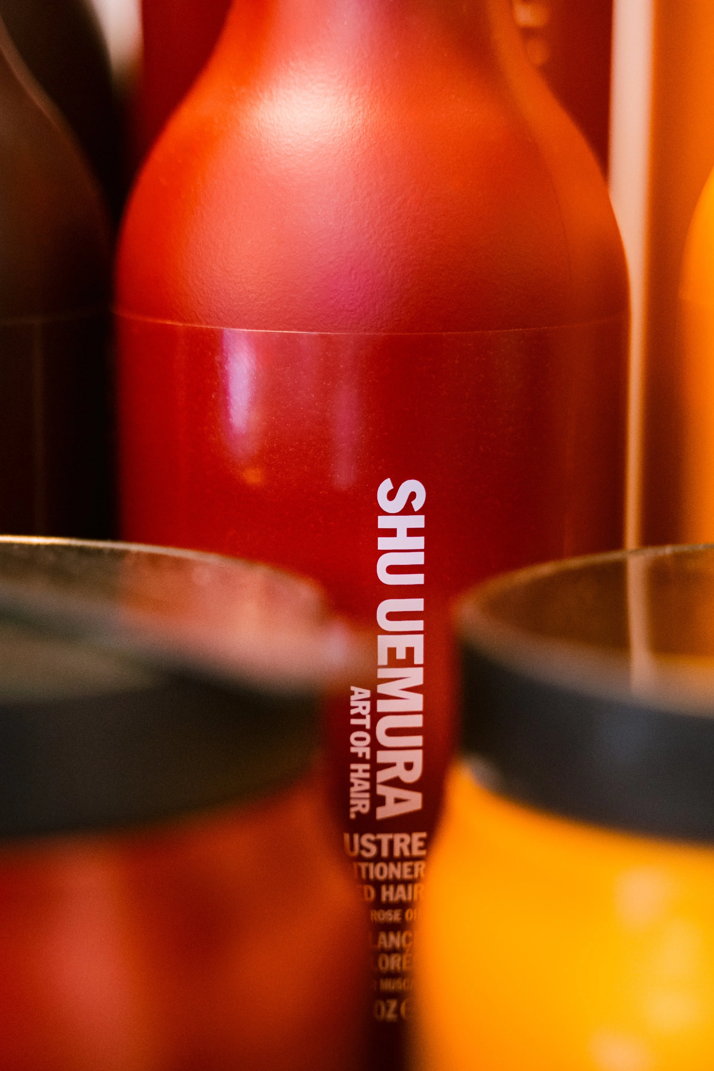 Photo d'un shampoing avec texte en anglais. Le flacon est principalement rouge avec du texte blanc et se trouve parmi d'autres flacons de couleurs différentes.