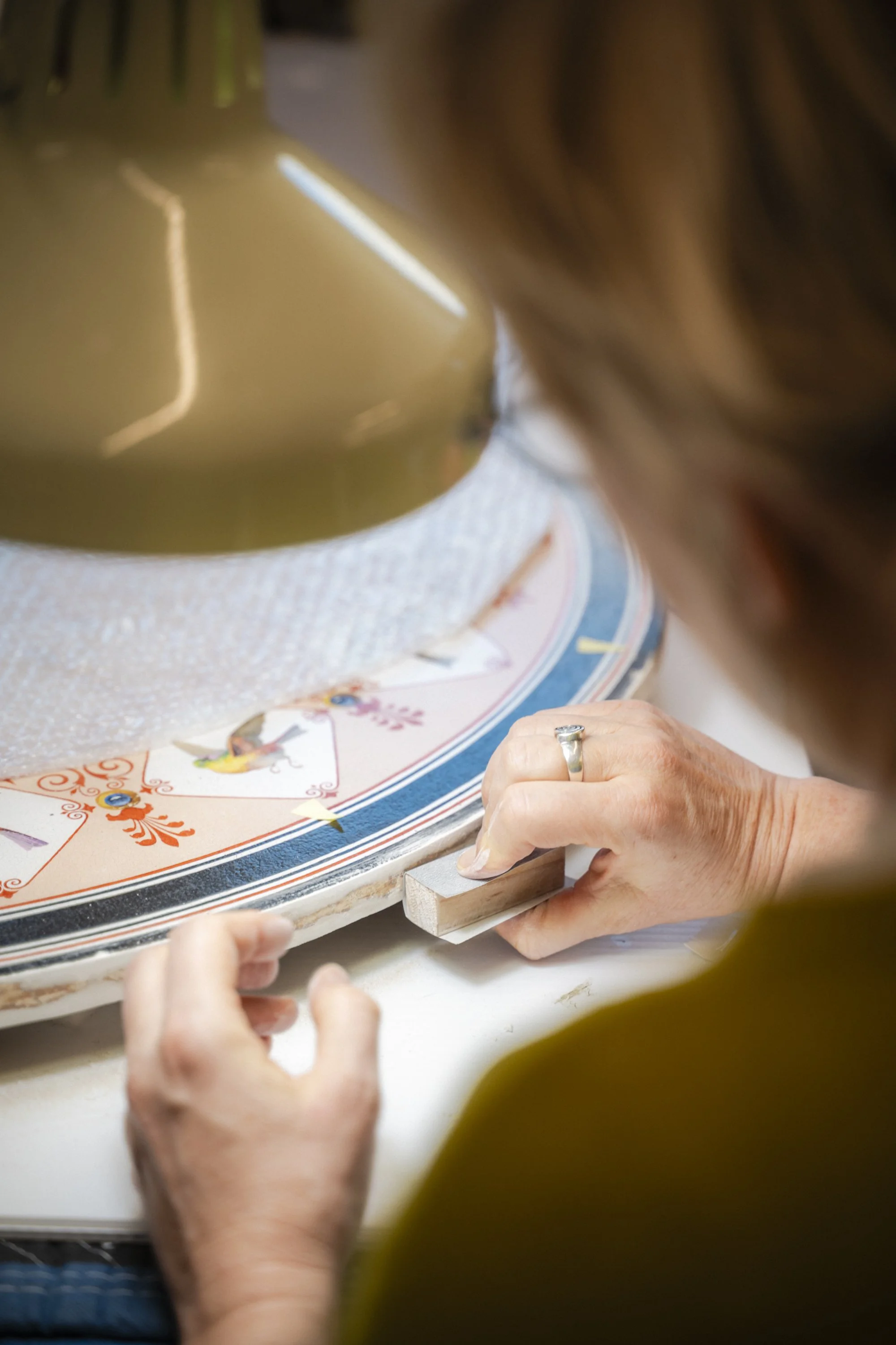 Une femme ponce un objet circulaire décoré de motifs colorés à la surface, probablement un objet artisanal.