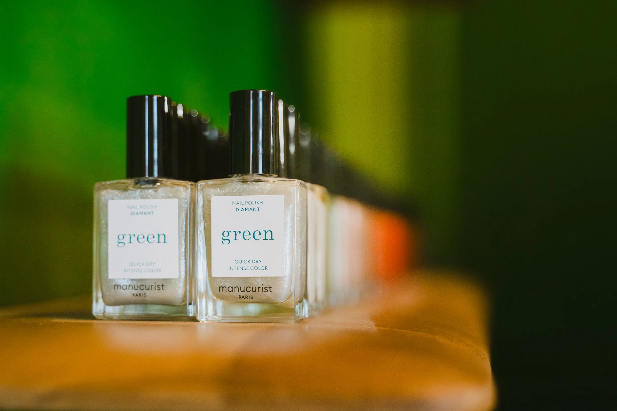 Flacons de vernis à ongles de couleur beige clair avec des bouchons noirs, affichant une étiquette avec la mention 'green' et 'Manucurist Paris'.
