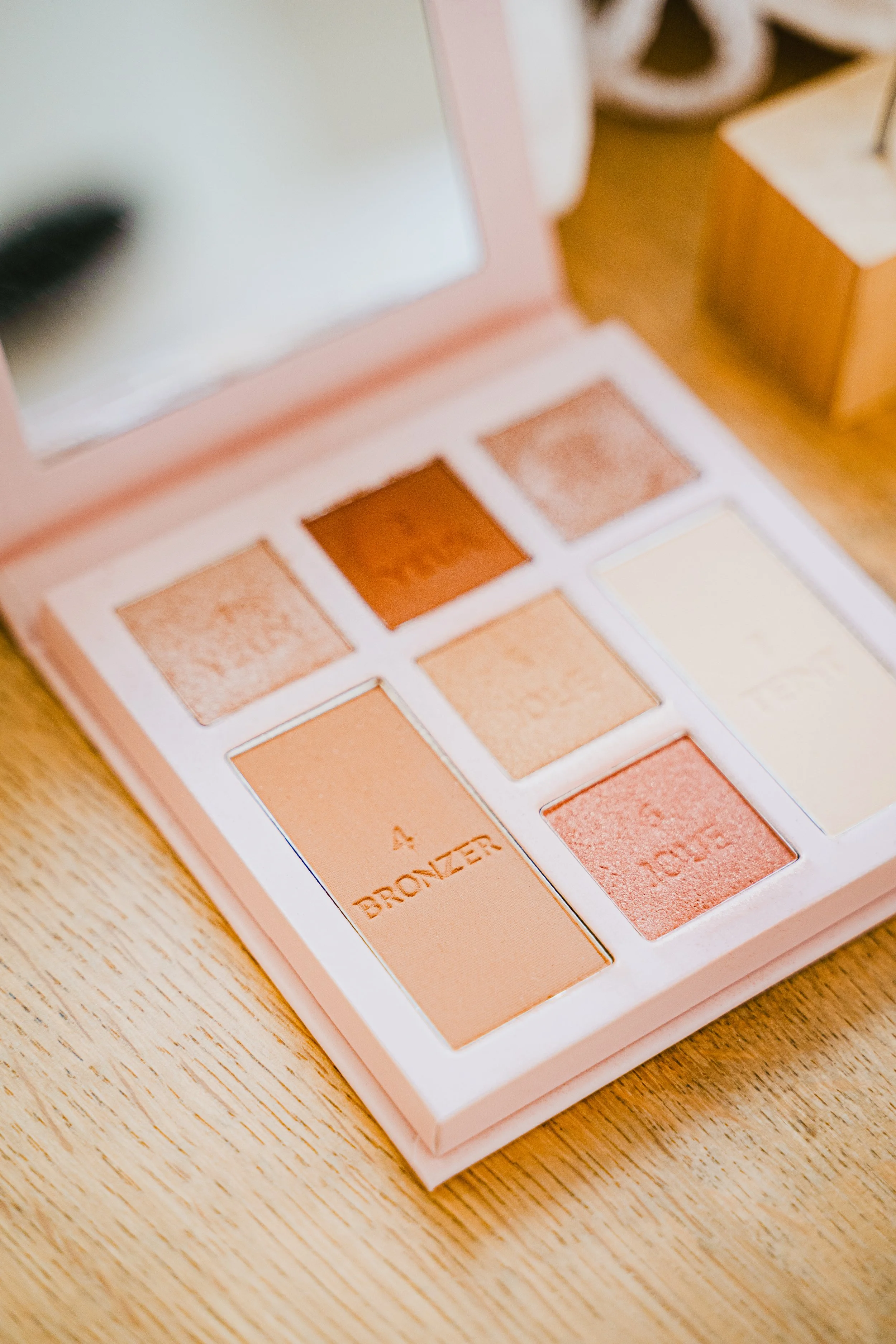 Palette de fards à paupières dans une boîte rose, posée sur une table en bois.