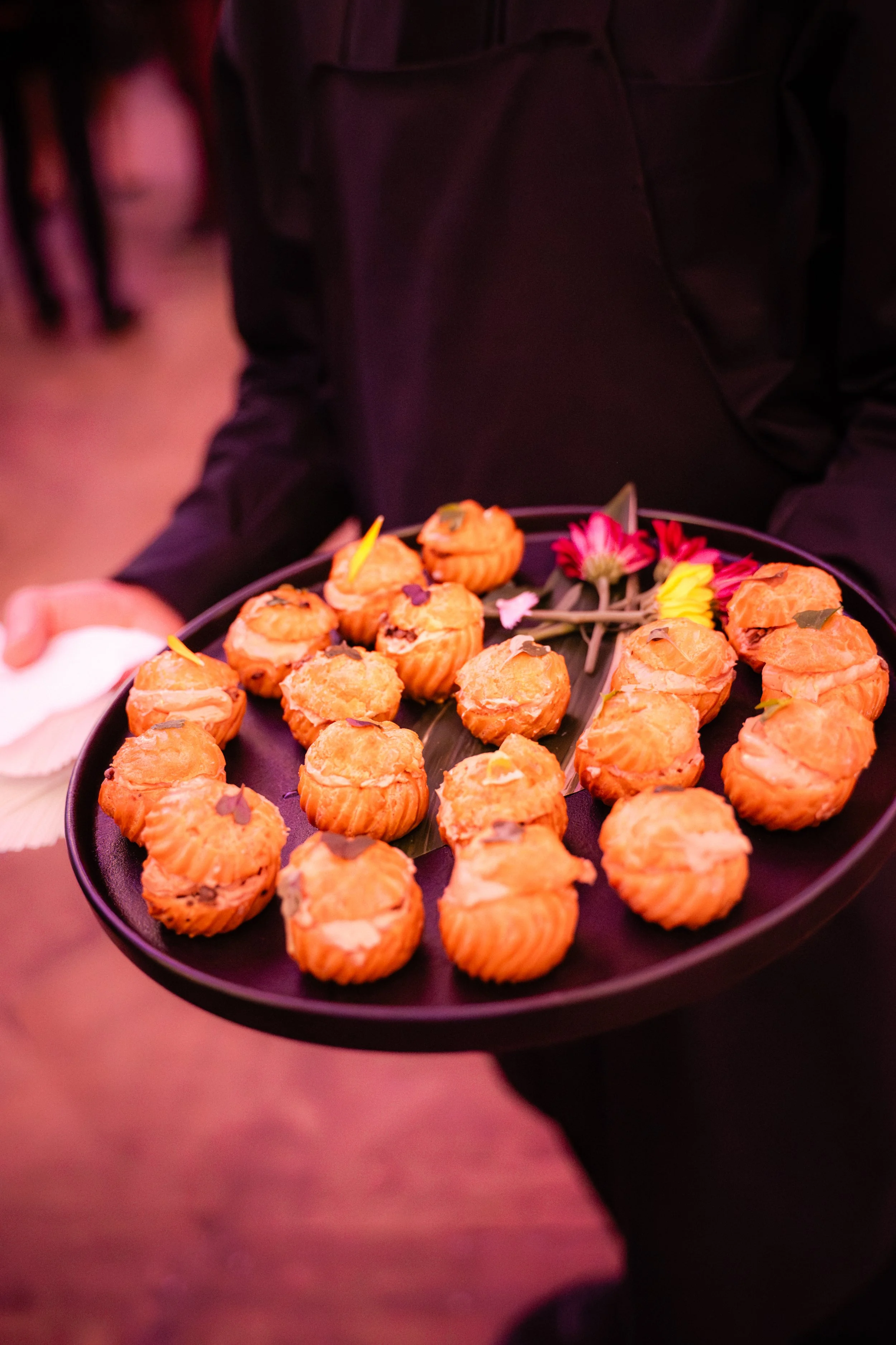 Gâteau de petits choux avec décoration florale tropicale, présenté sur un plateau noir, dans une ambiance de fête ou événement.