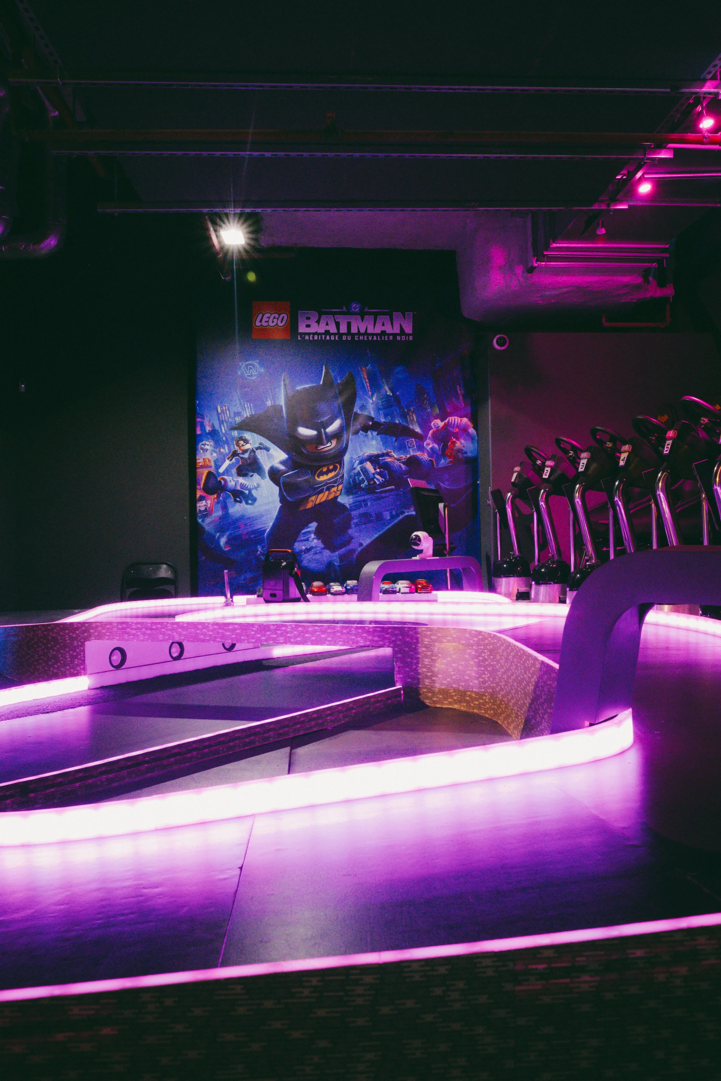 Salle de karting avec un poster de LEGO Batman et des sièges, éclairage violet et scène futuriste