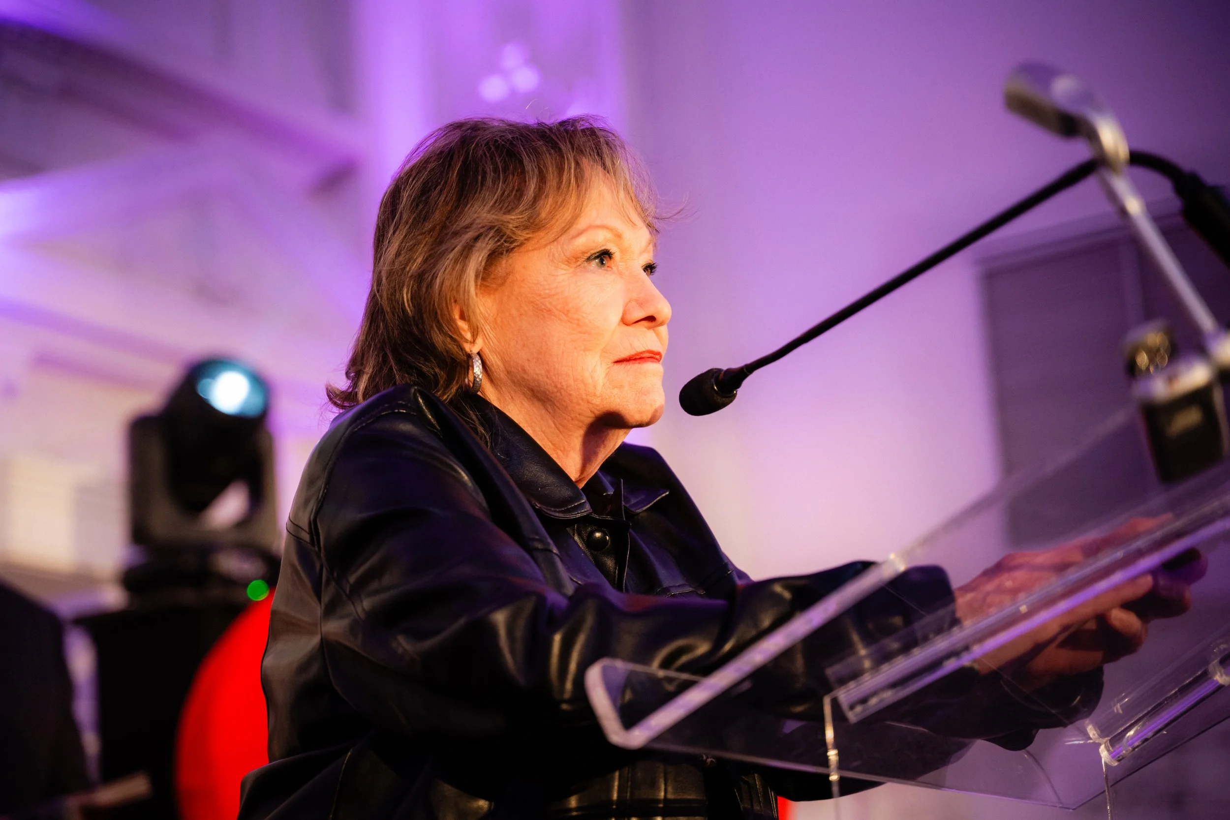 Une femme donne un discours solennel avec un éclairage violet en arrière-plan.