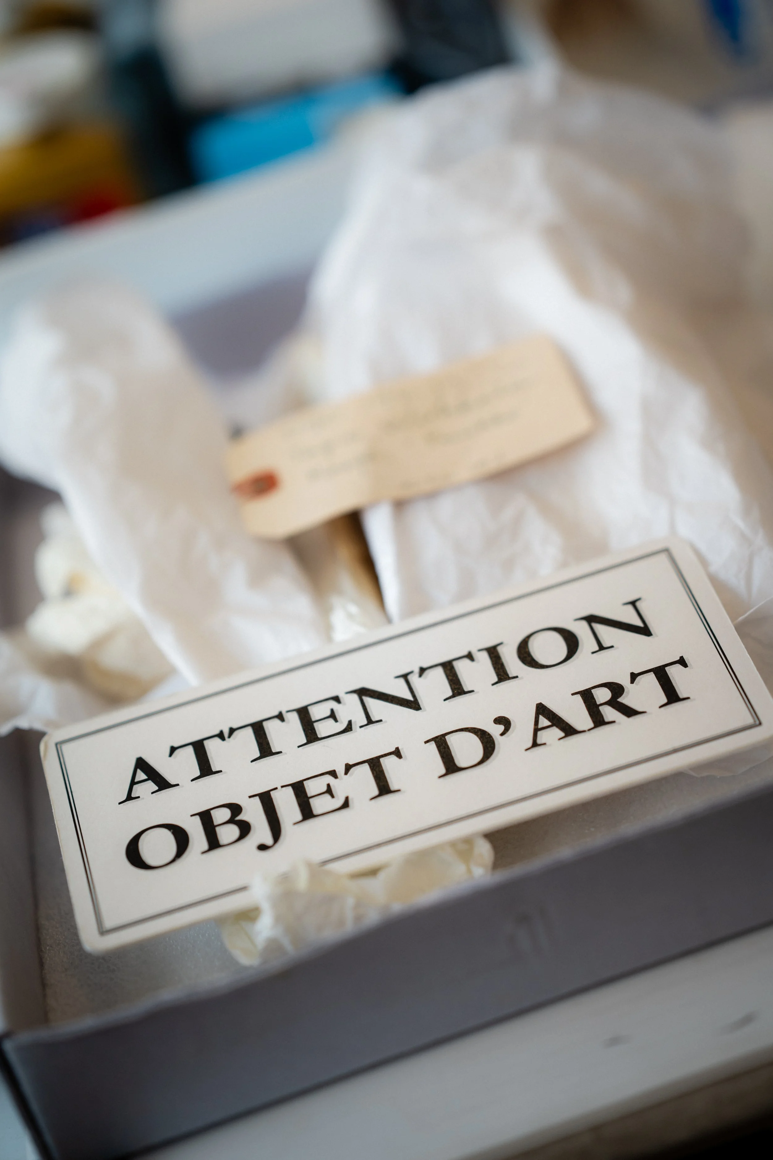 Une boîte avec une étiquette en français qui dit "Attention Objet d'art", contenant du papier blanc et une carte.