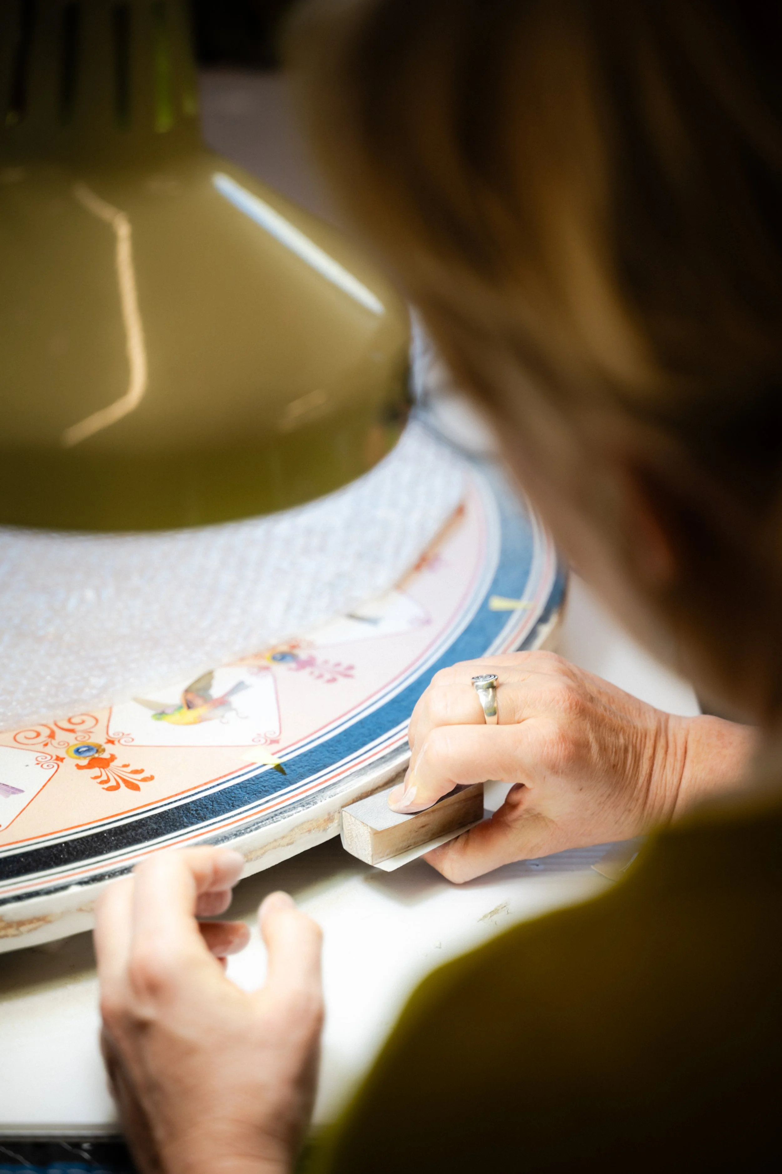 Une personne utilise un burin pour travailler un objet circulaire décoré de motifs colorés à la surface, probablement un objet artisanal.