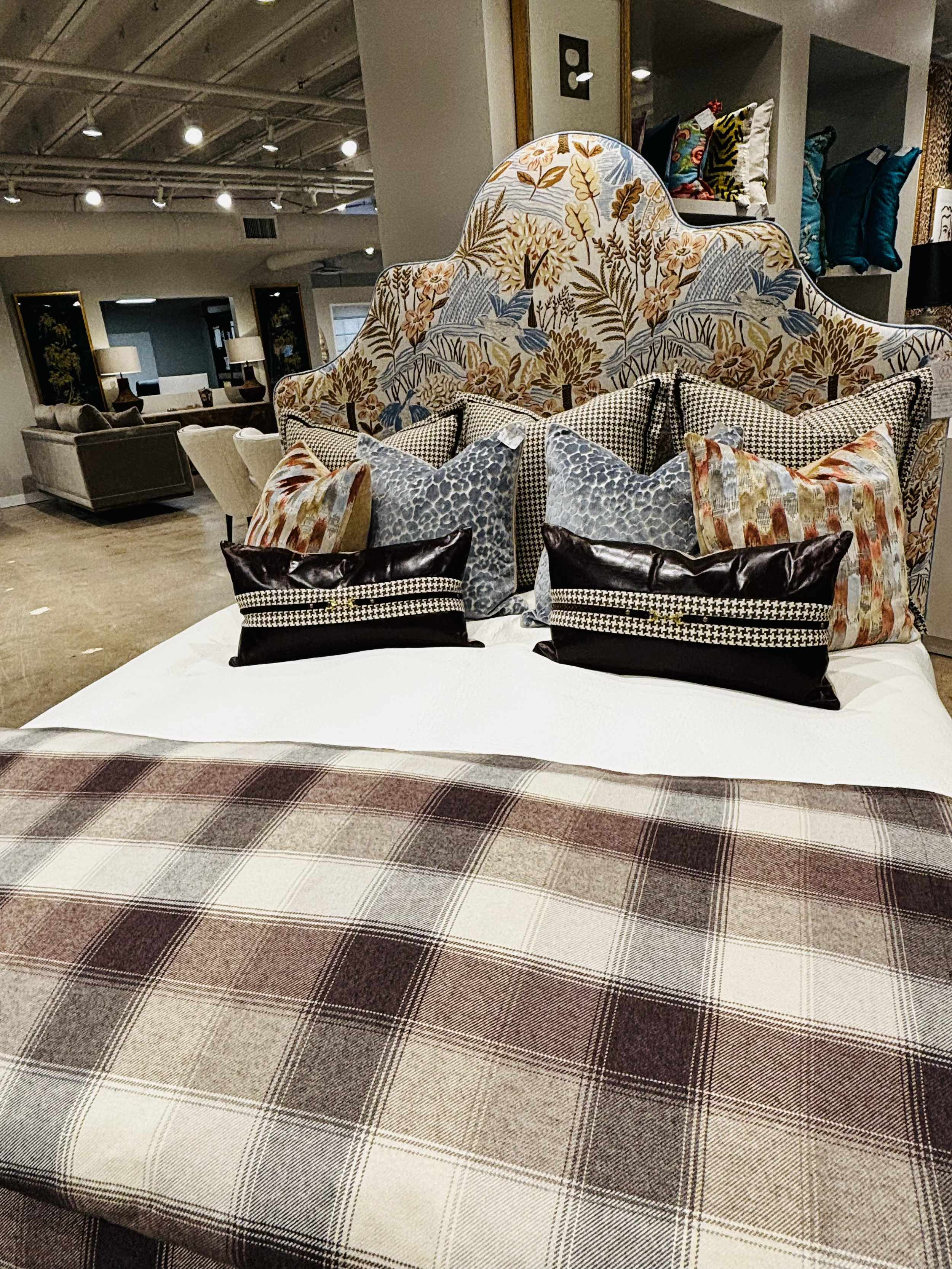 Display of various decorative pillows on a furniture piece in a home decor store with a plaid carpeted floor in the foreground.