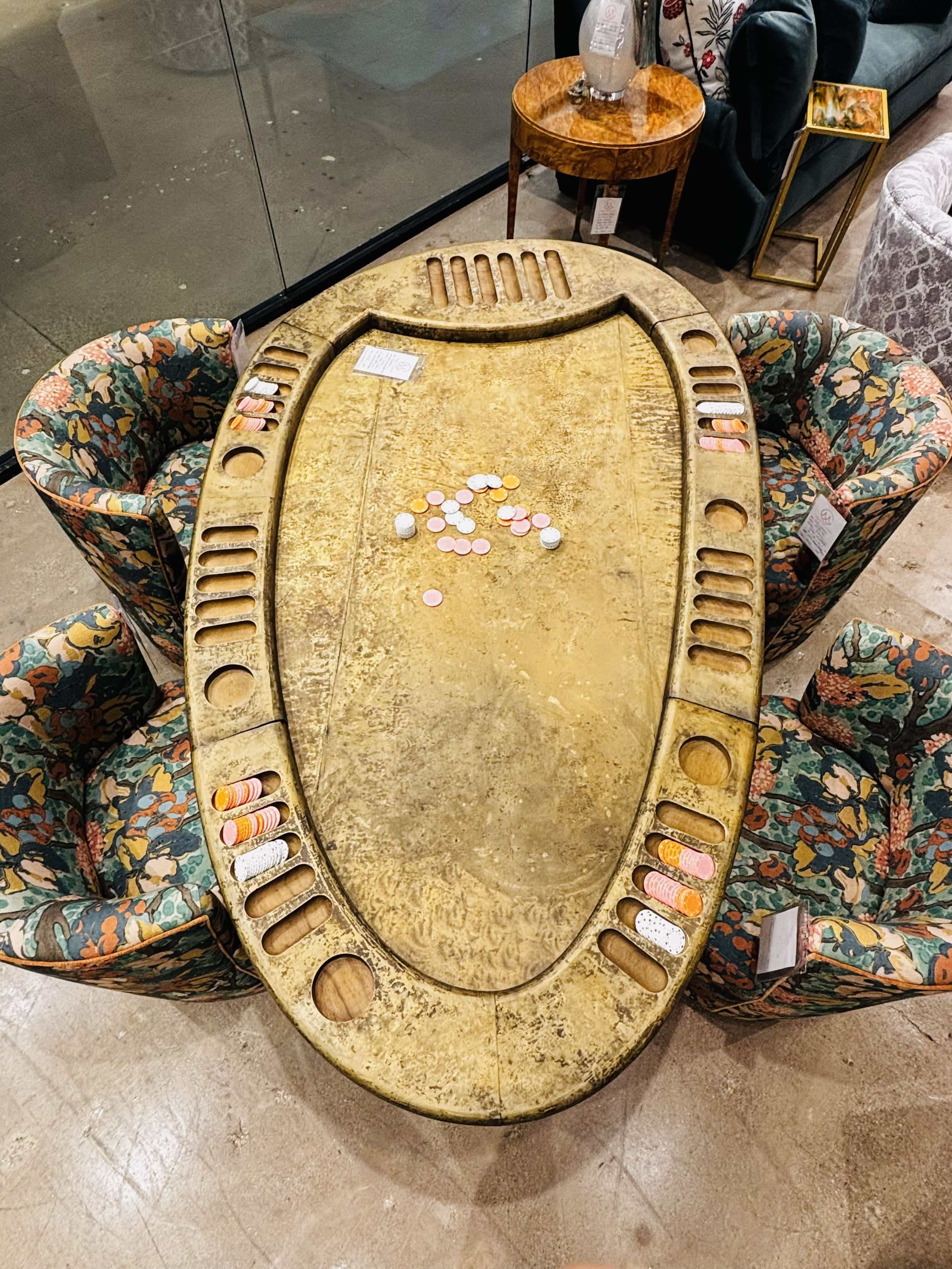 A poker table with colorful, patterned chairs surrounding it, scattered with poker chips and some coins.