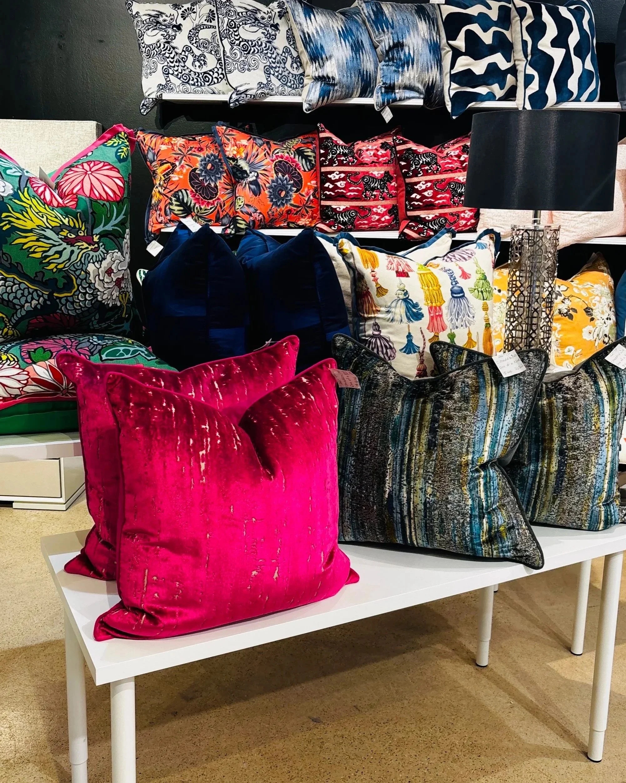 Display of various decorative pillows with vibrant colors and patterns on a white table in a store.