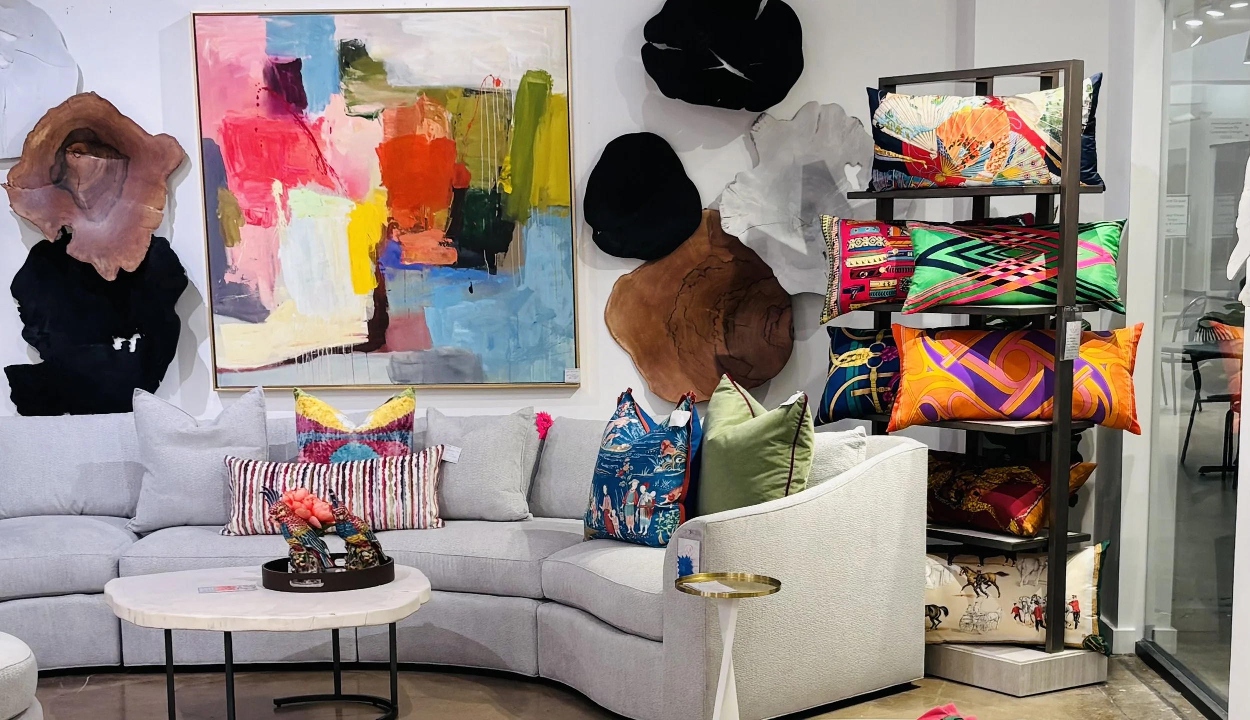 Display of colorful home decor including painted wall art, decorative pillows, and abstract wooden sculptures in a furniture store.