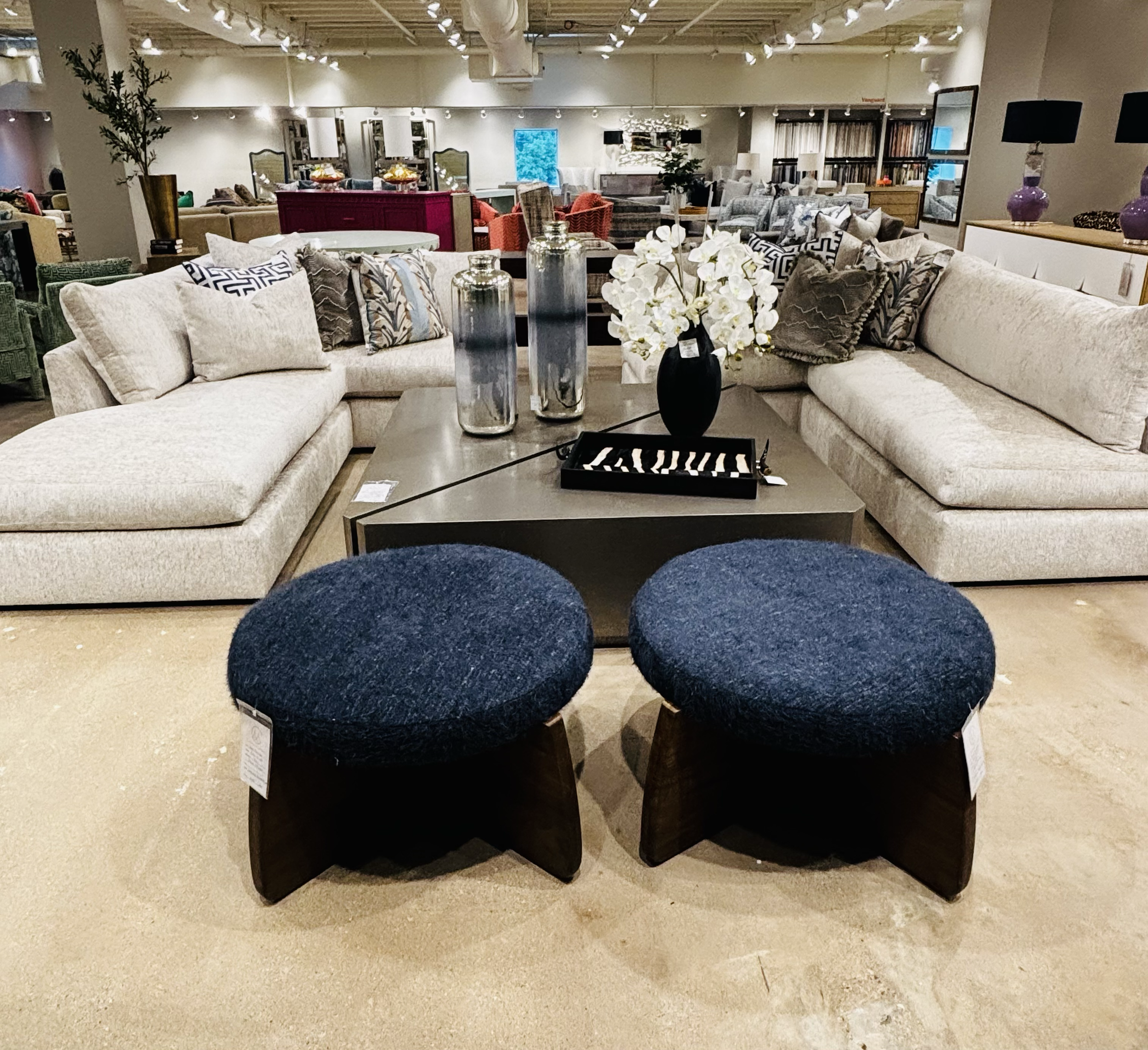 A furniture store displays sofas, chairs, and decorative items like vases and flowers in a well-lit, spacious layout.