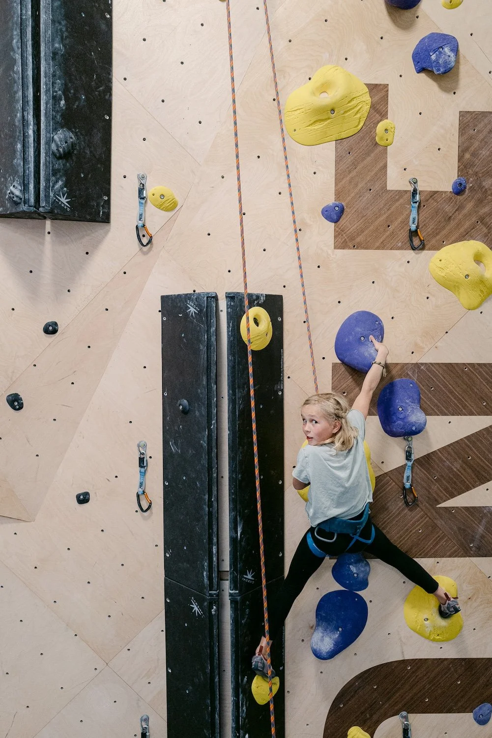 Young girl climbing on ropes on an indoor rock climbing wall with colorful climbing holds.