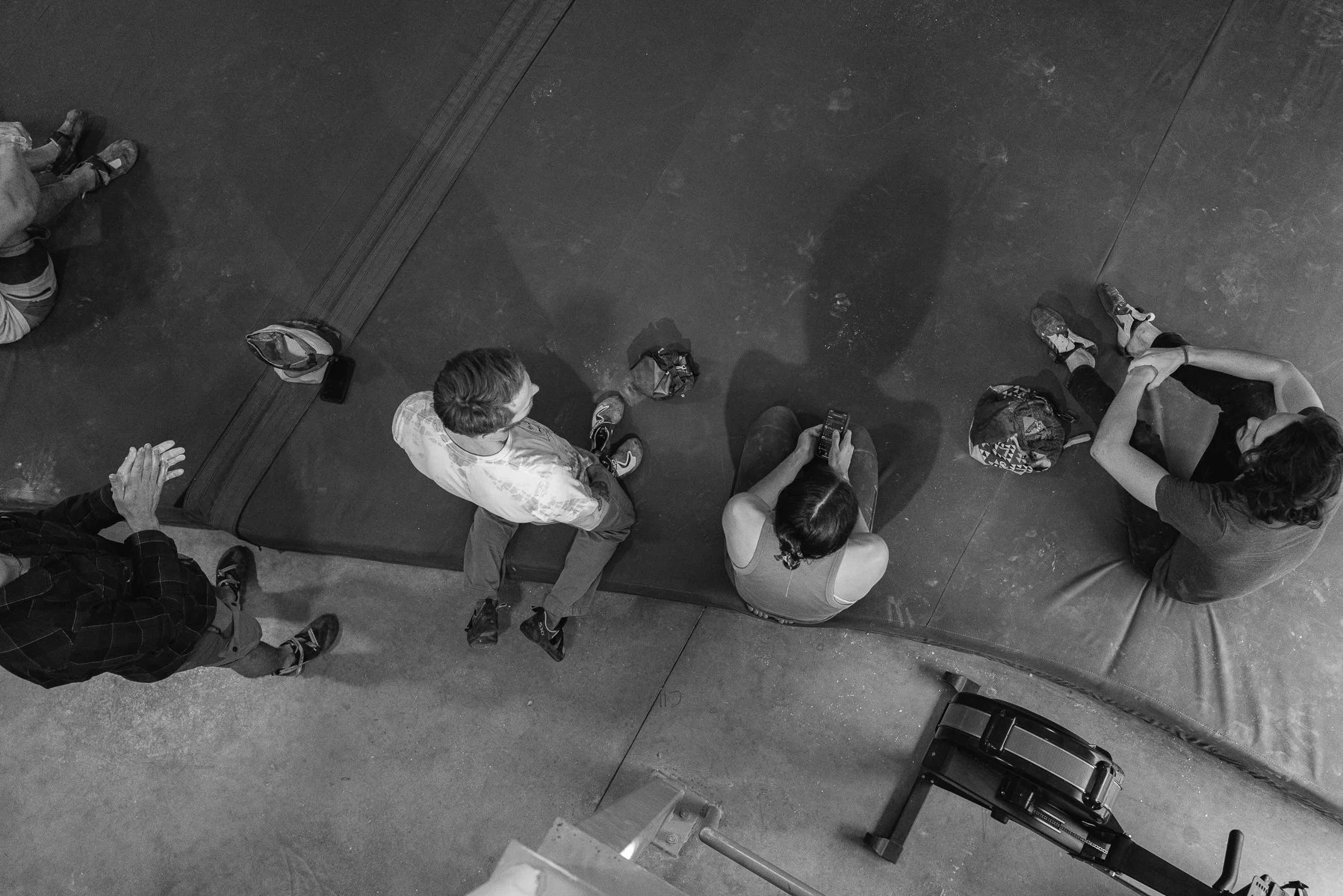 Black and white image of climbers hanging out on a bouldering pad.