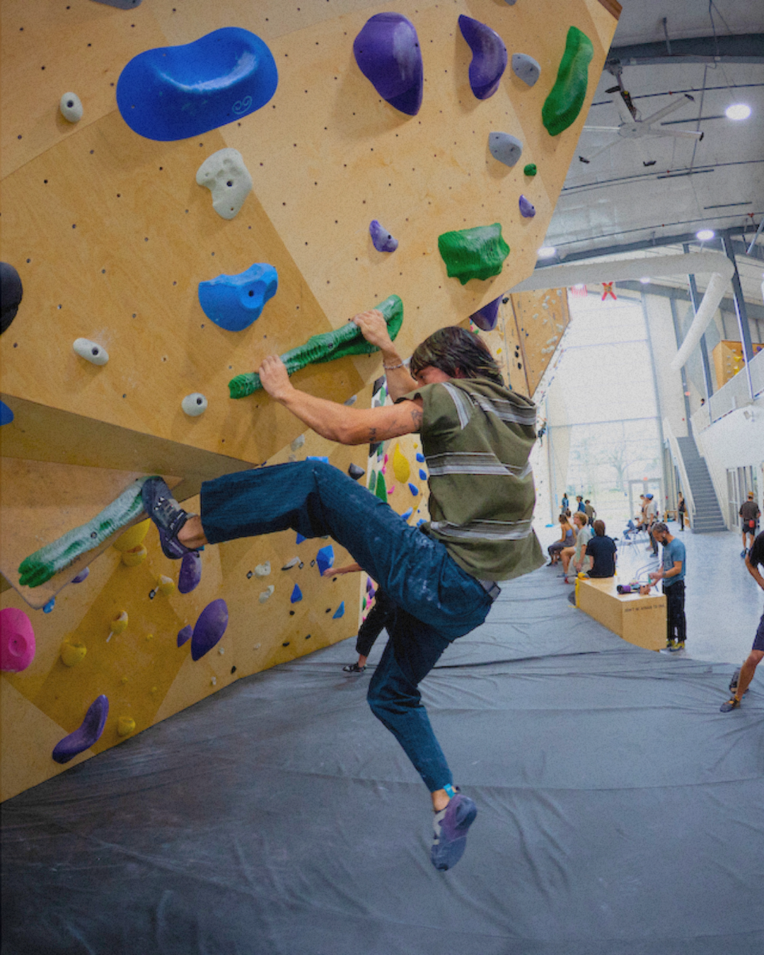 Person attempting to climb an indoor bouldering wall in a gym.