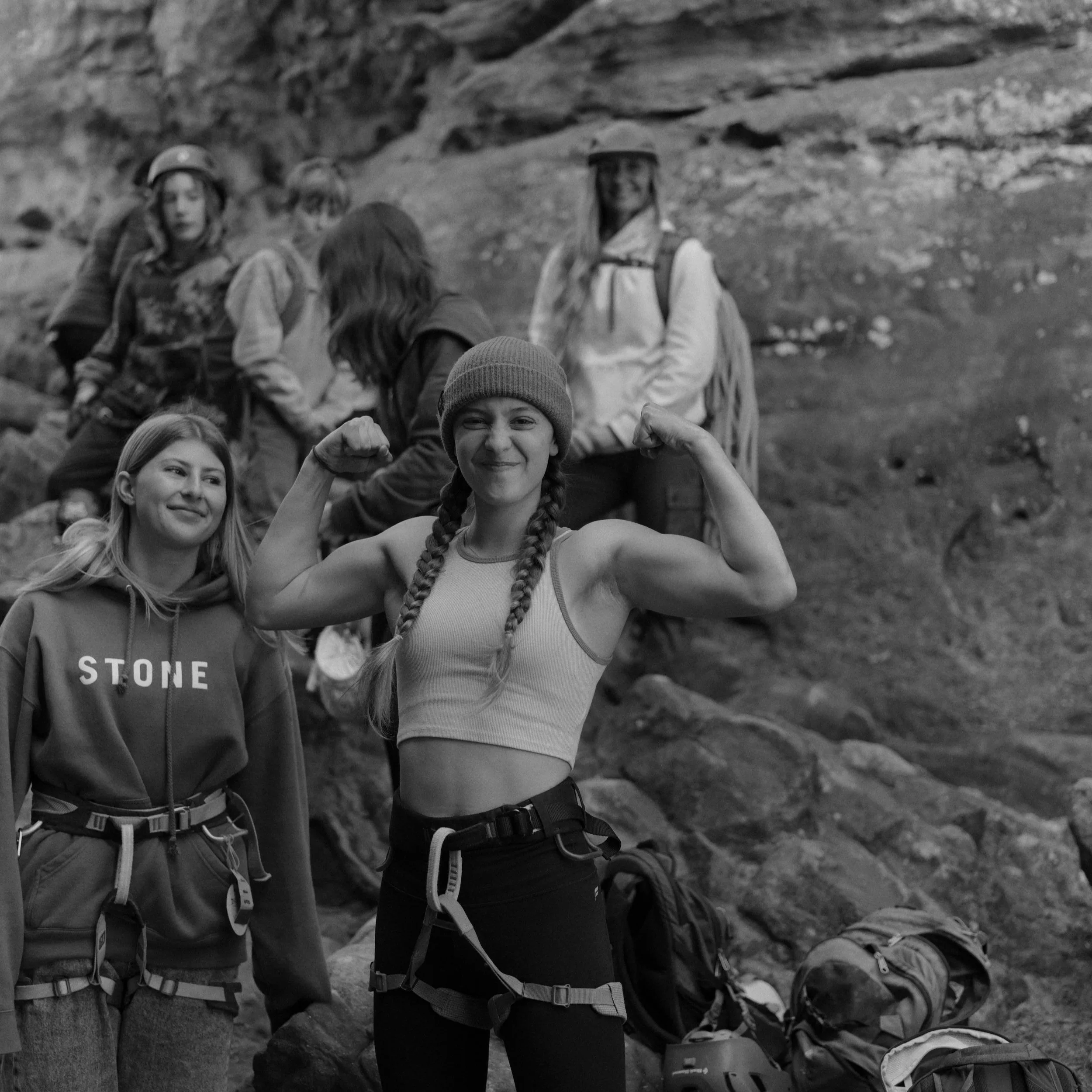 A group of young people hiking outdoors, some wearing backpacks and outdoor gear, with a rocky landscape in the background.