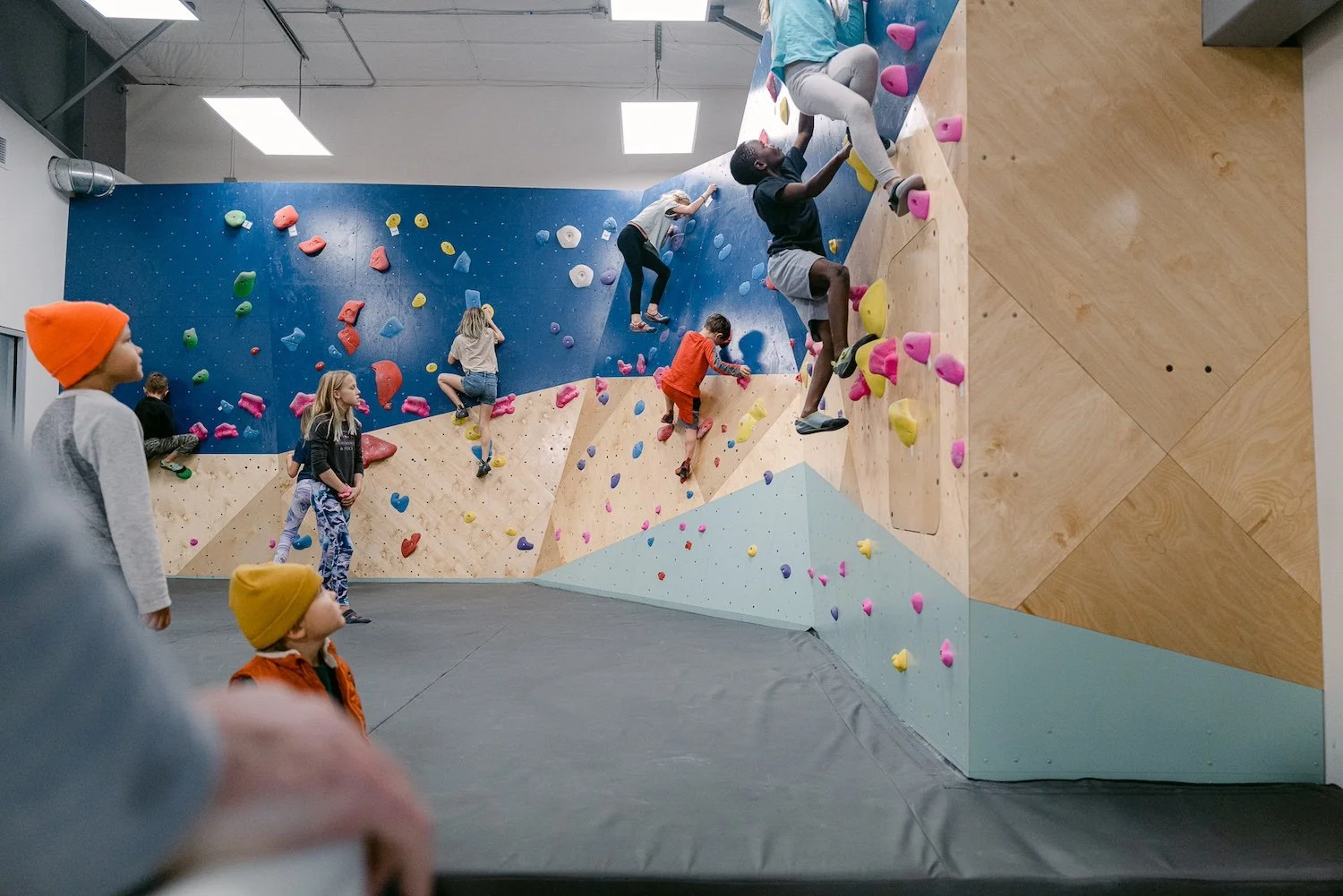 Kids bouldering on a colorful bouldering wall at an indoor climbing gym.