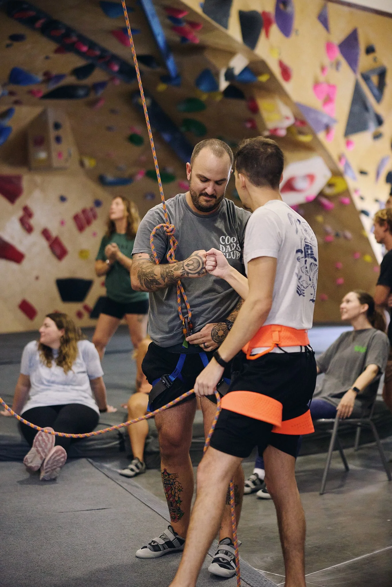 Two people fist bumping while tied into a climbing rope. One is a rock climbing instructor teaching a class at a climbing gym.