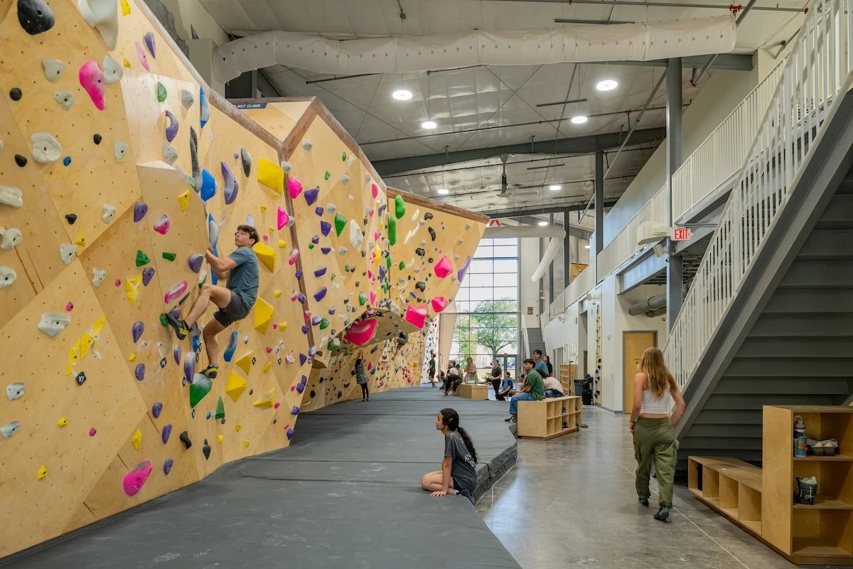 Indoor rock climbing gym with people bouldering on walls with brightly colored holds.