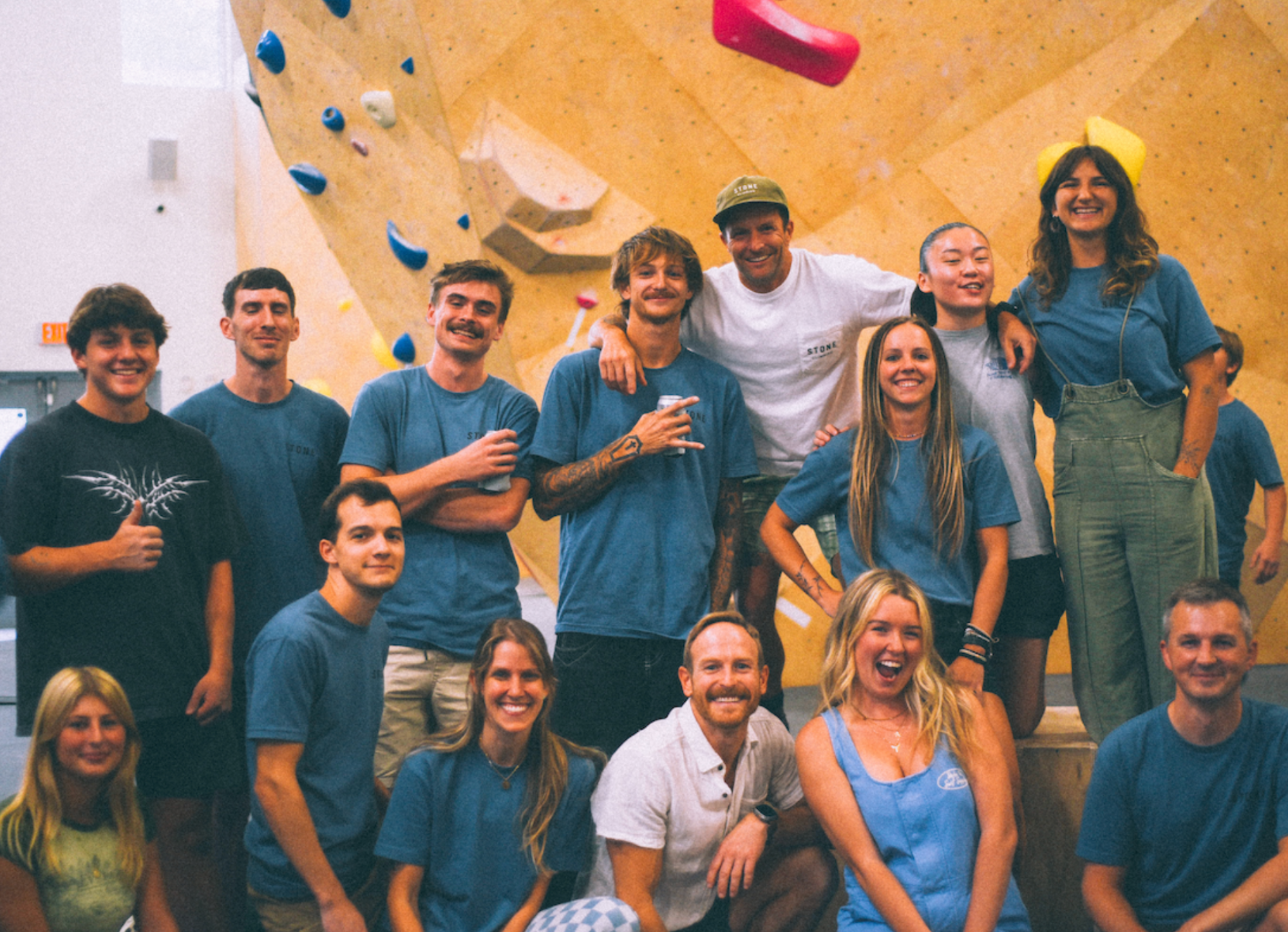 Group of smiling people posing in front of an indoor climbing wall.
