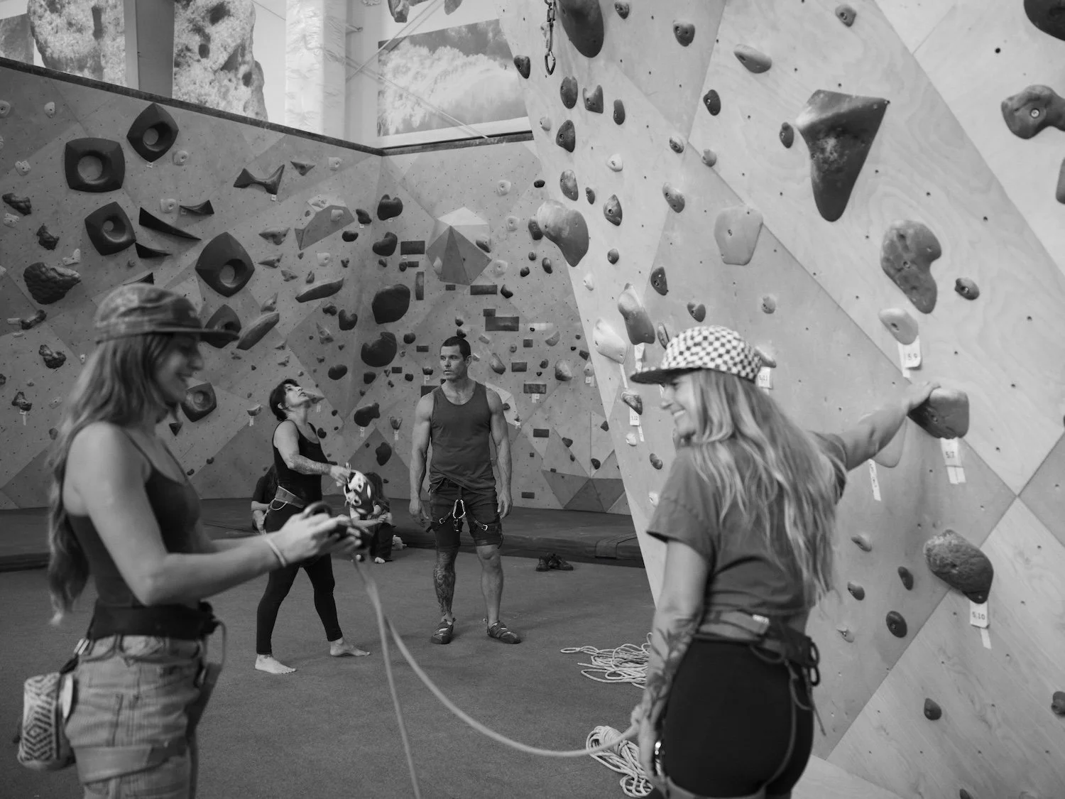 Black and white image of pretty girls climbing ropes and an in shape man with bouldering walls in the background.