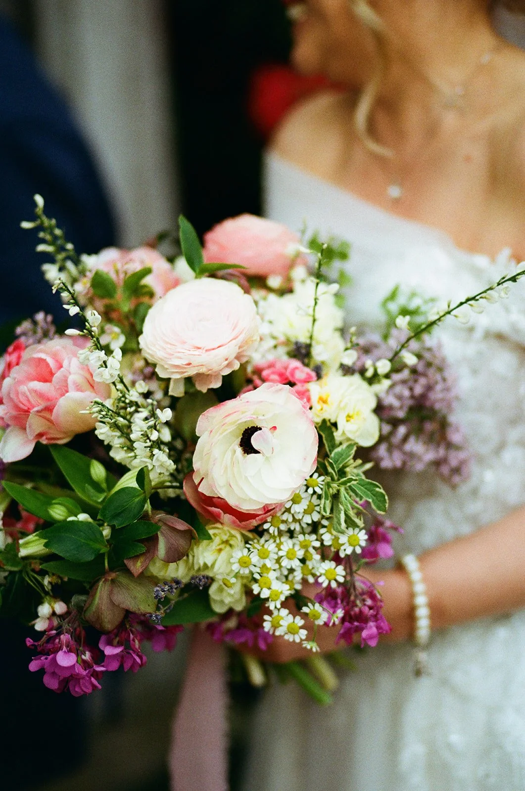 Bride holding a colorful bouquet of pink, white, and purple flowers during a wedding ceremony.