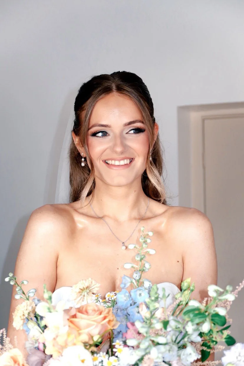 A smiling young woman in a wedding dress with a bouquet of flowers.