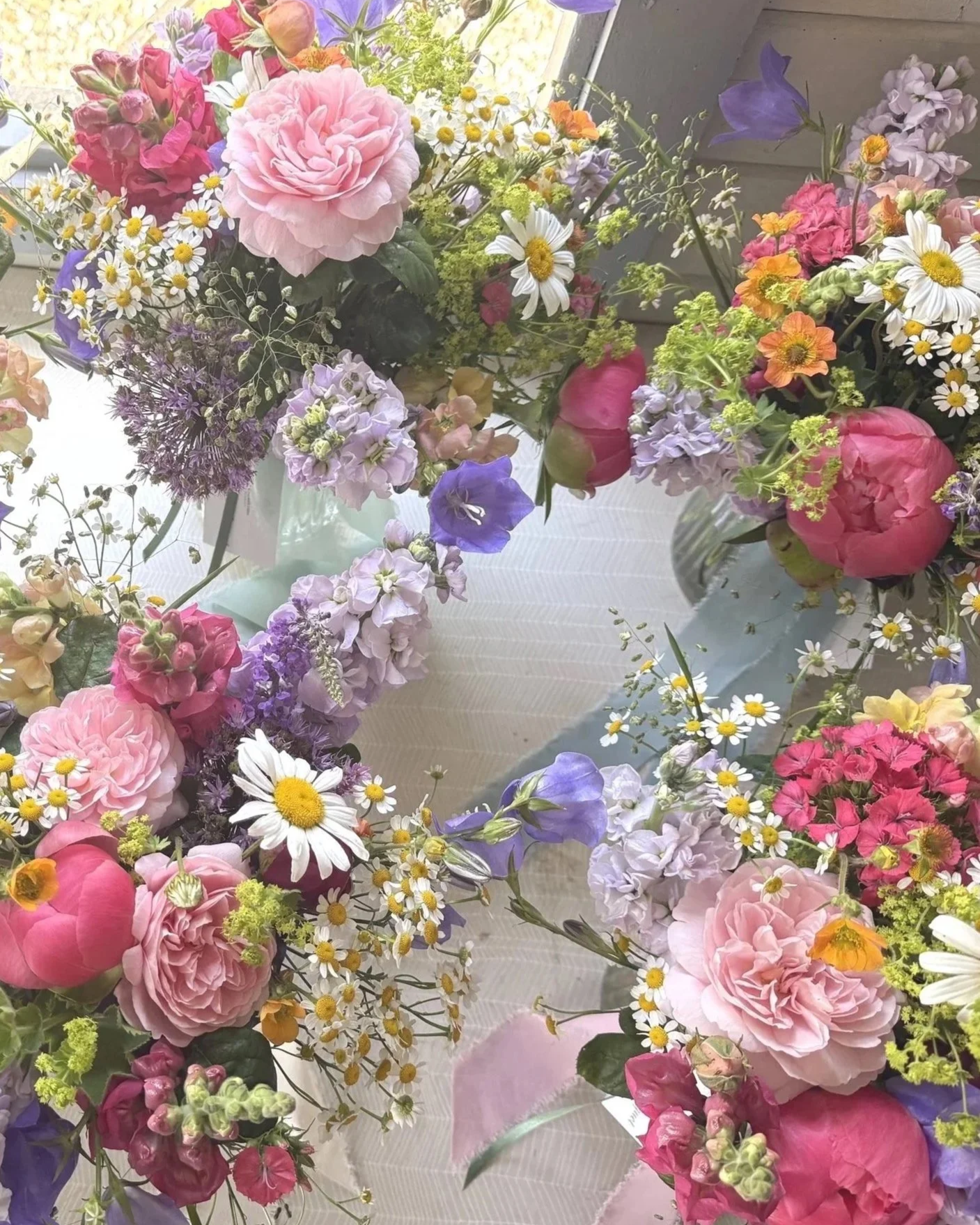 A variety of colorful fresh flowers arranged in bouquets, including pink roses, daisies, purple and pink blooms, and small orange and yellow flowers, placed on a table near a window.