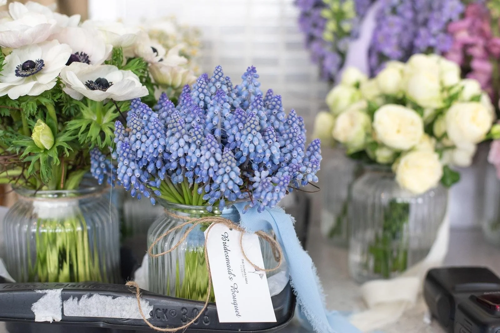 4 different bridesmaids bouquets each made exclusively with a different flower, one is white anemones, one blue Muscari, one roses, one Delphinium
